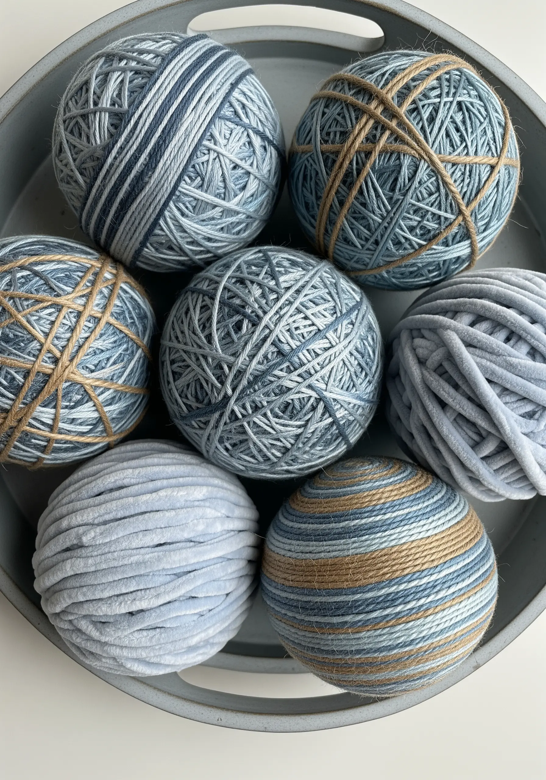 A collection of decorative balls wrapped in various shades of blue and tan yarn and jute.