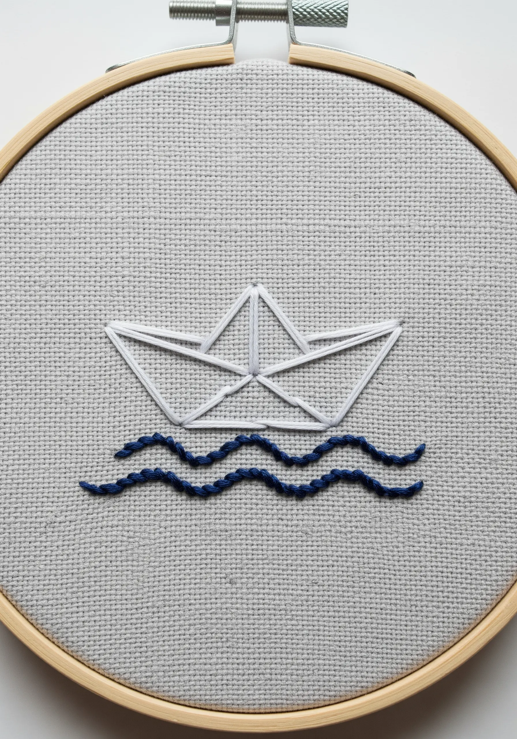 A minimalist paper boat in white backstitch floating on wavy blue stem stitch waves.