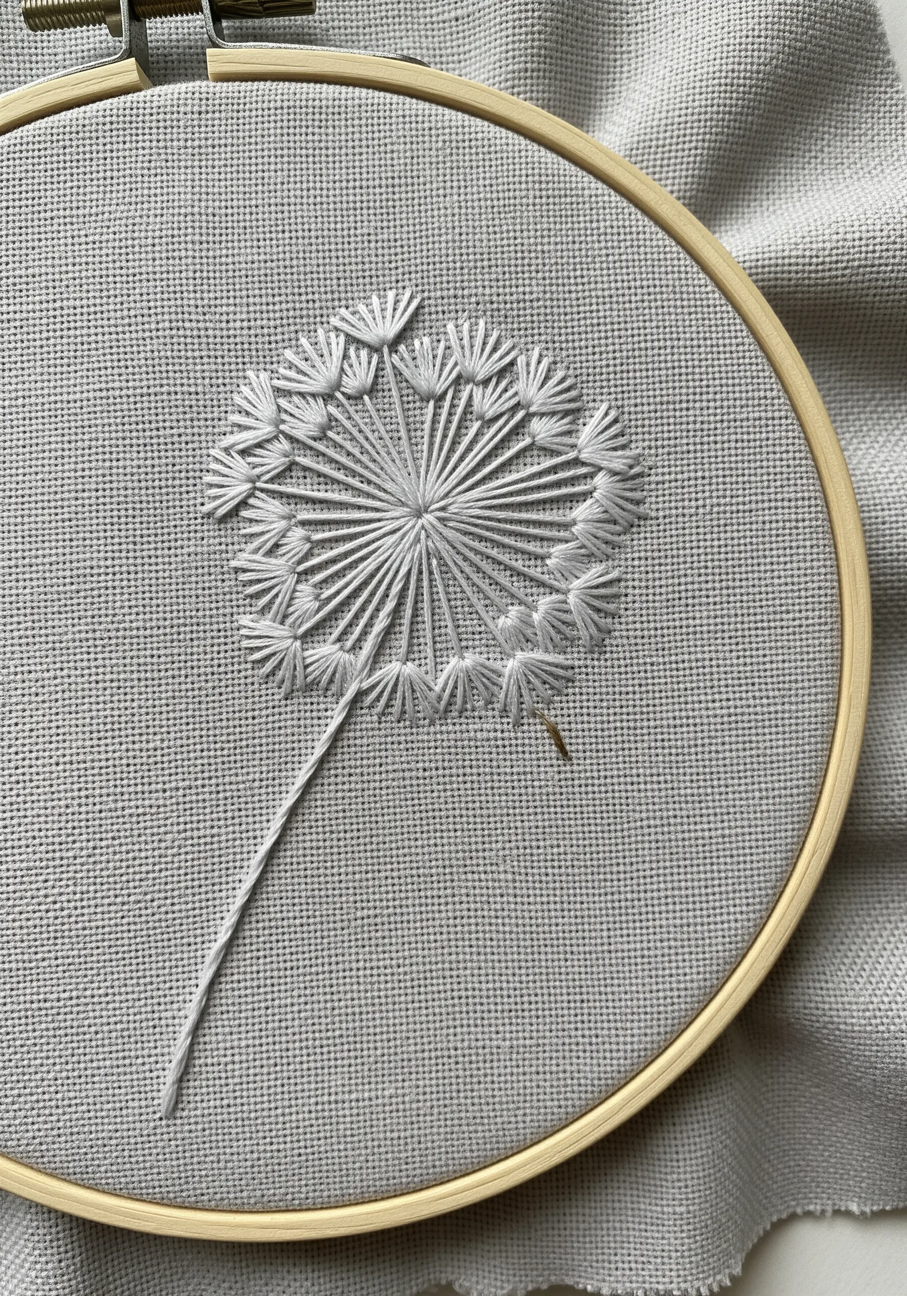 A white dandelion head embroidered with radiating straight and detached chain stitches.