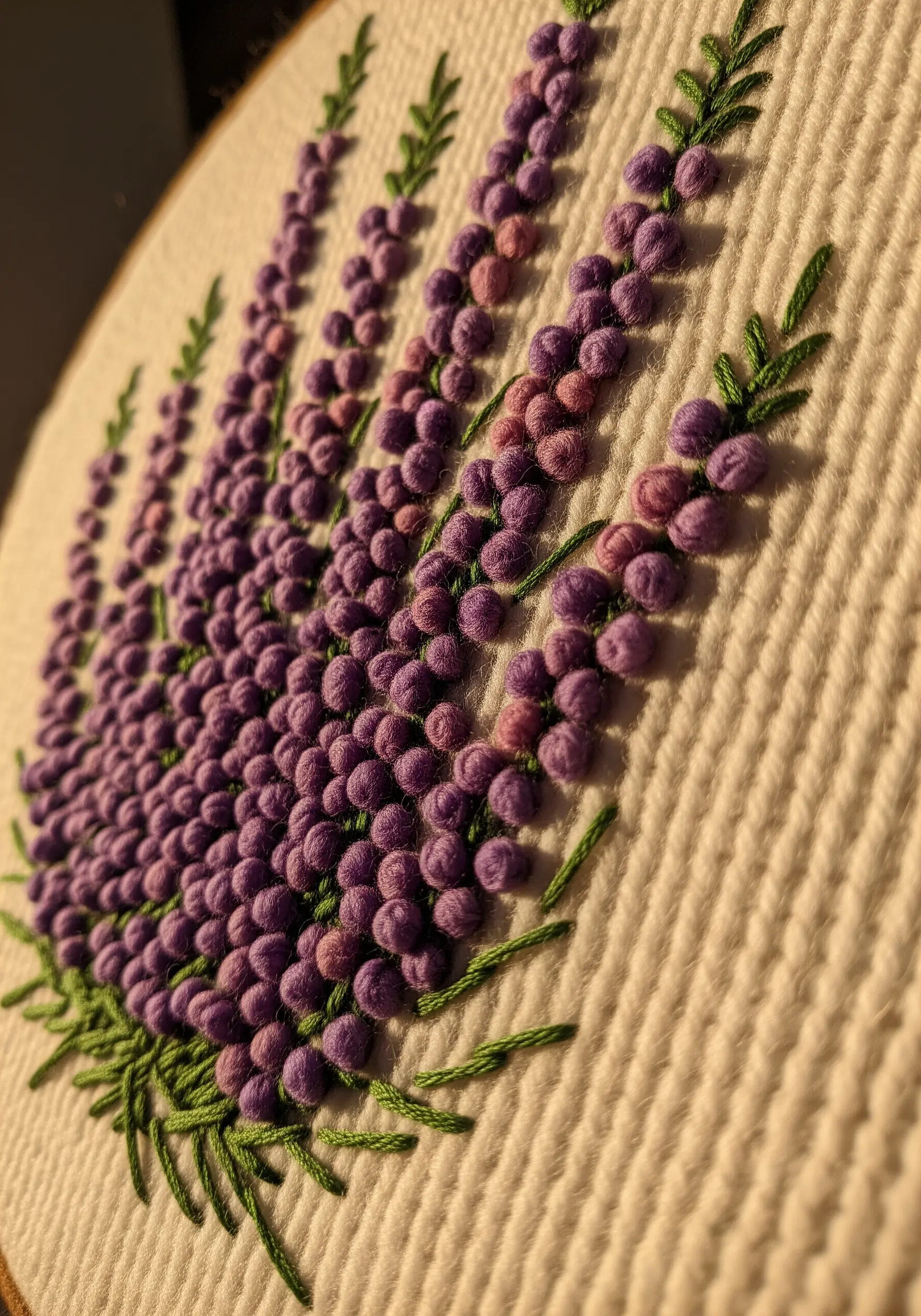 A close-up of dense purple French knots creating a textured lavender or lupine flower.