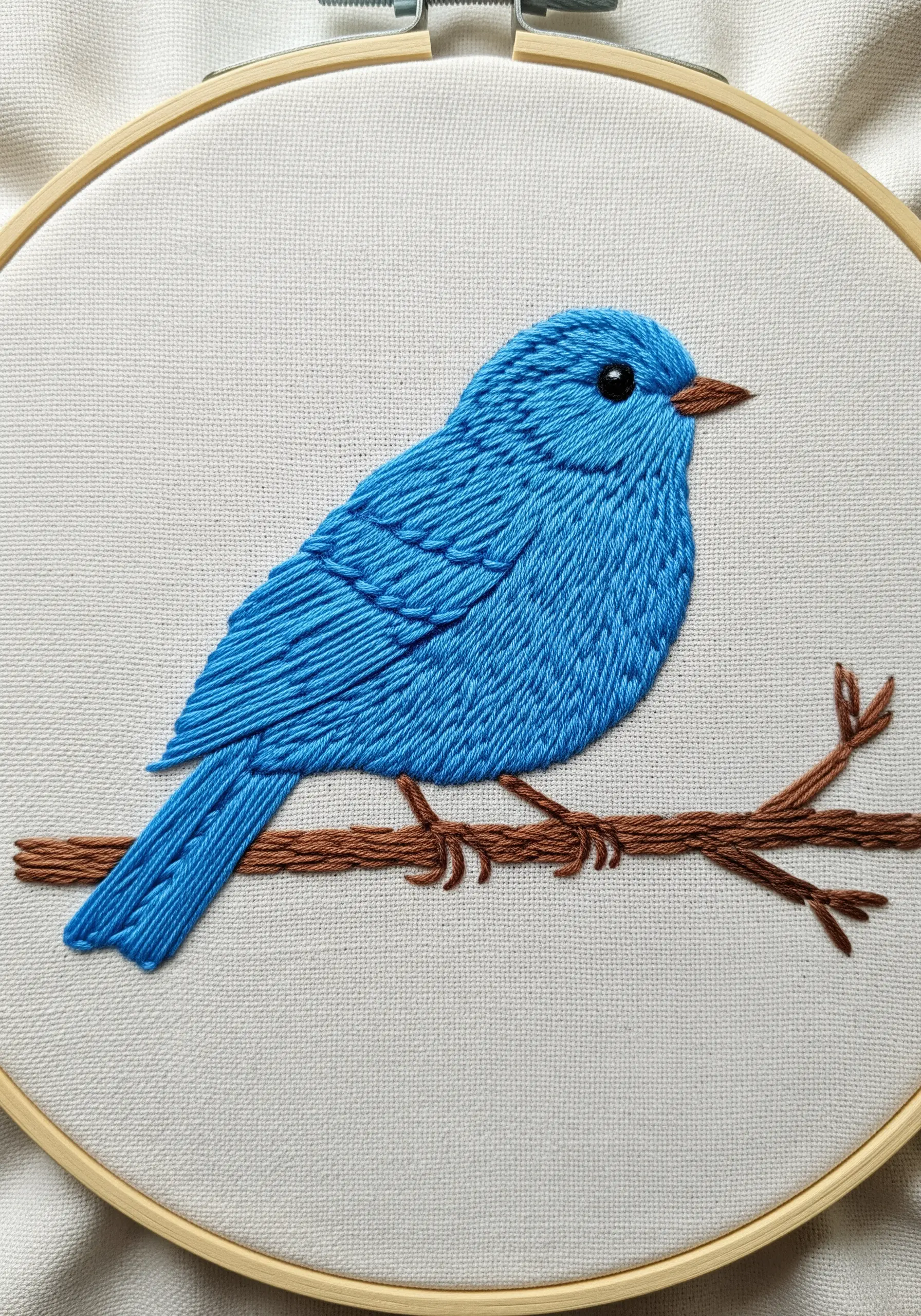 A bright blue bird embroidered with layered sections of satin stitch.