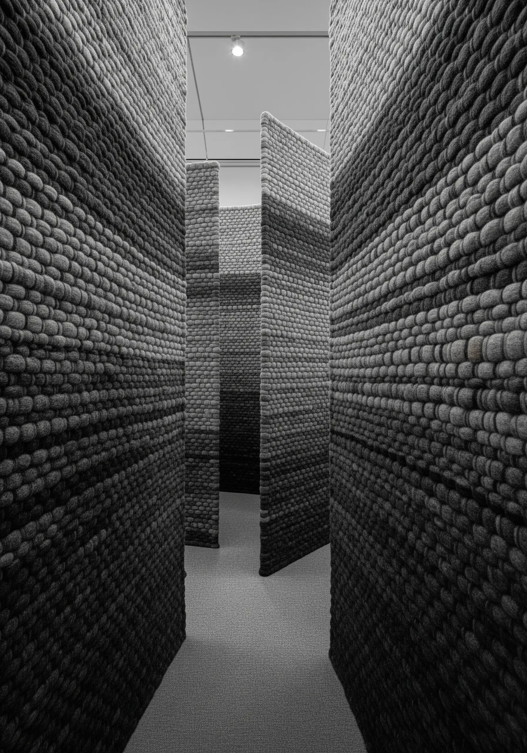 A maze-like installation with walls made of thick, woven gray wool in varying shades.