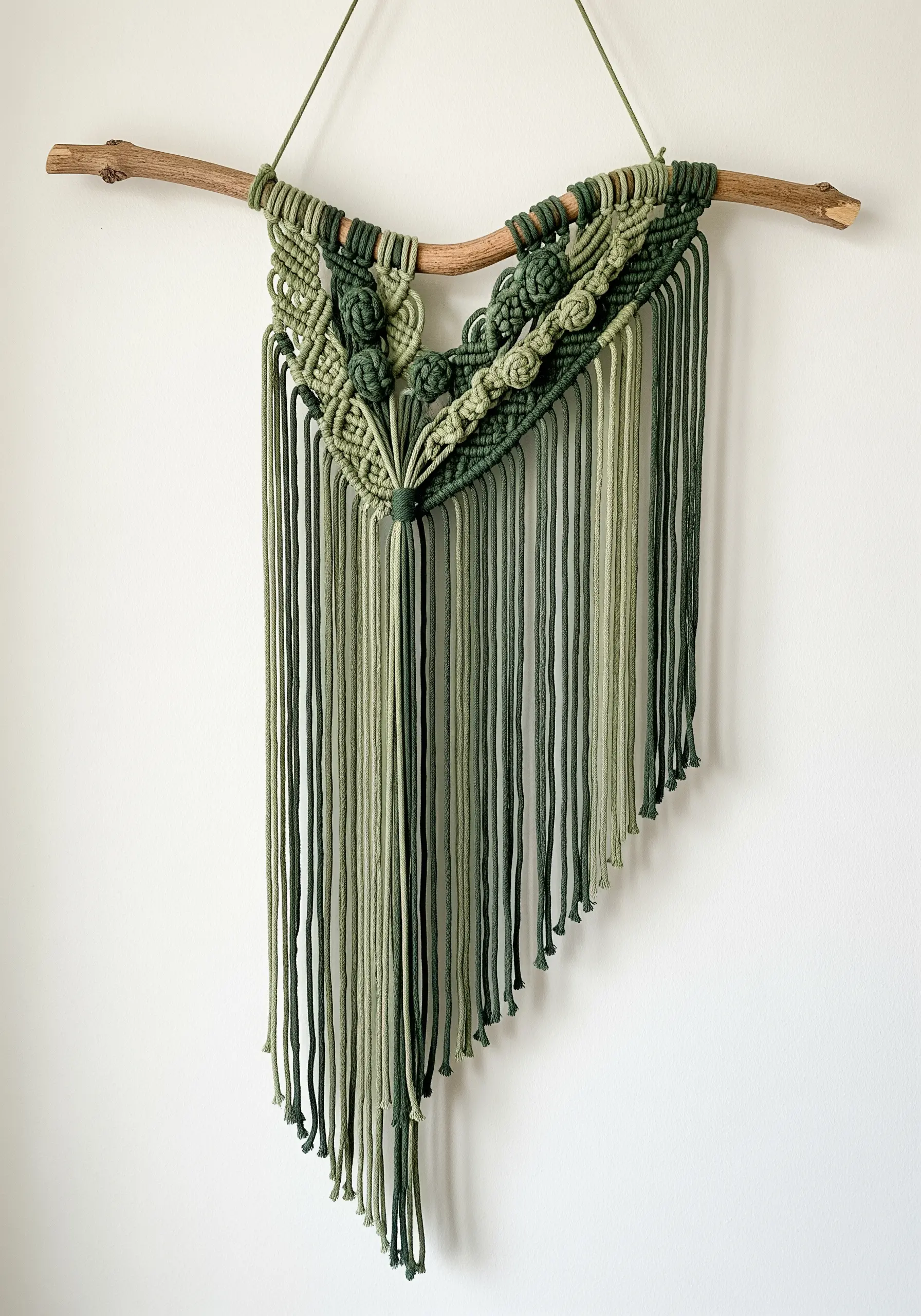 Macrame wall hanging using different shades of green yarn and various knot textures.