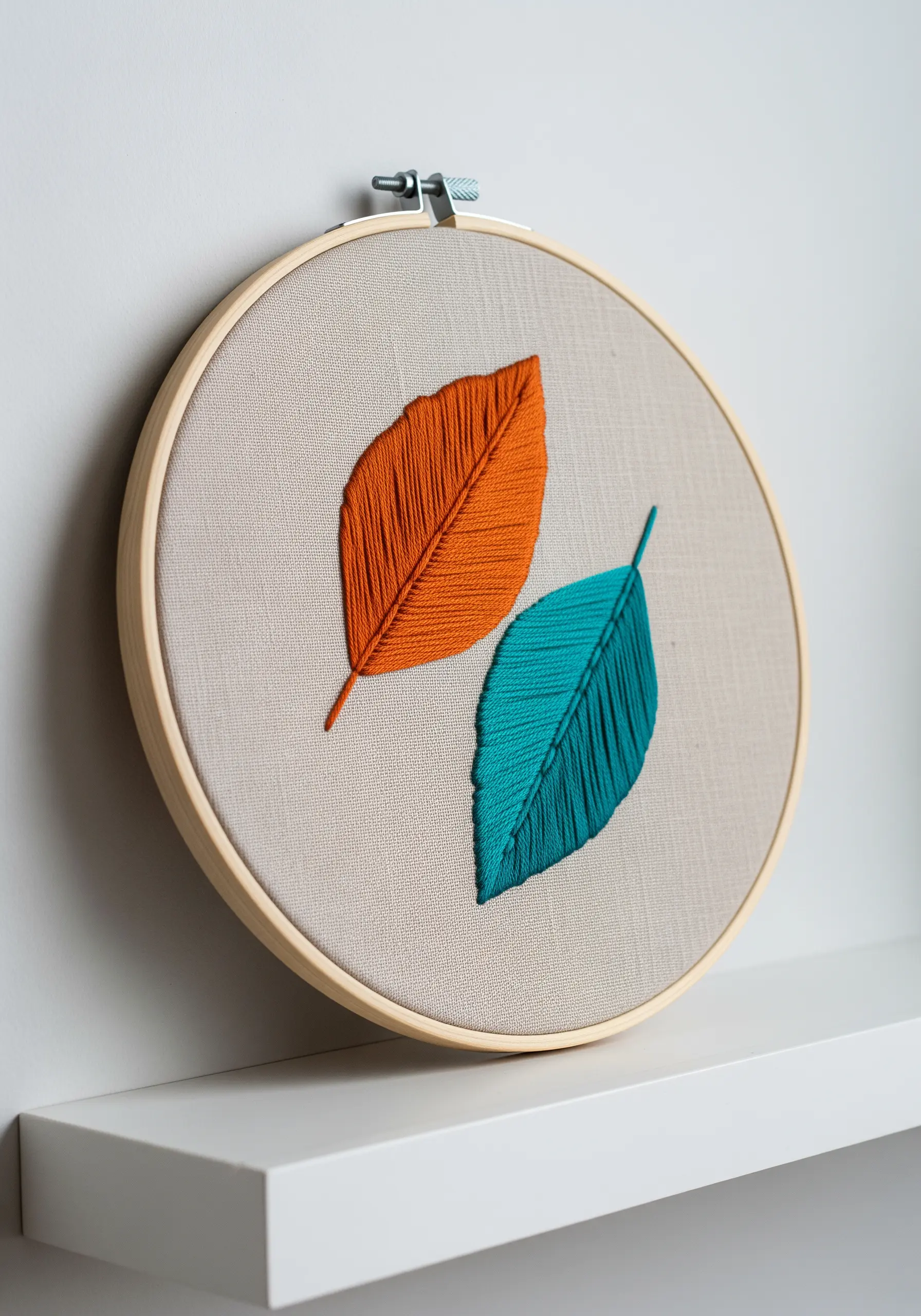 Two embroidered leaves, one in solid orange and one in solid teal, on neutral fabric.