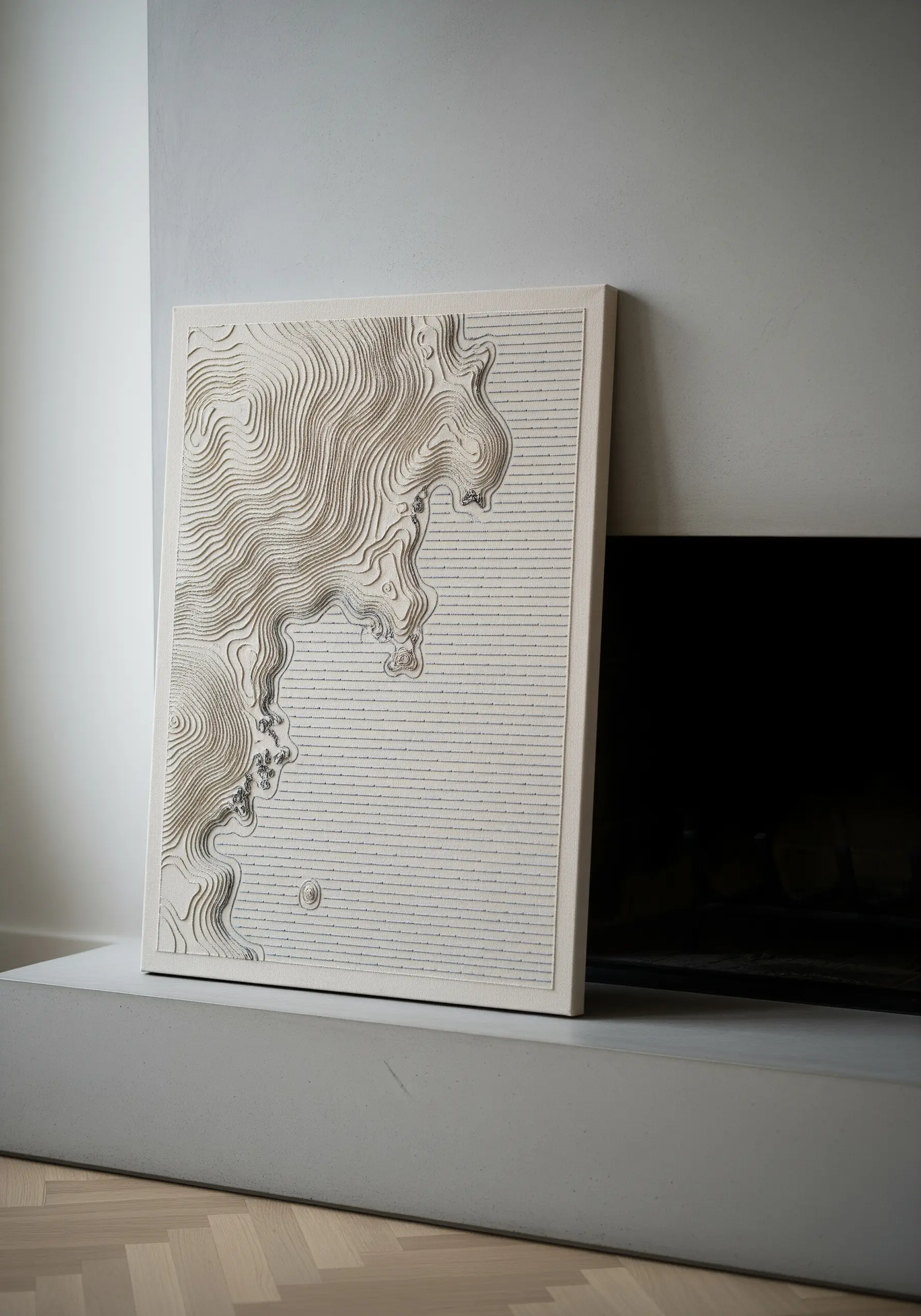 Framed embroidery of a topographical map with dense, textural contour lines in a neutral color.