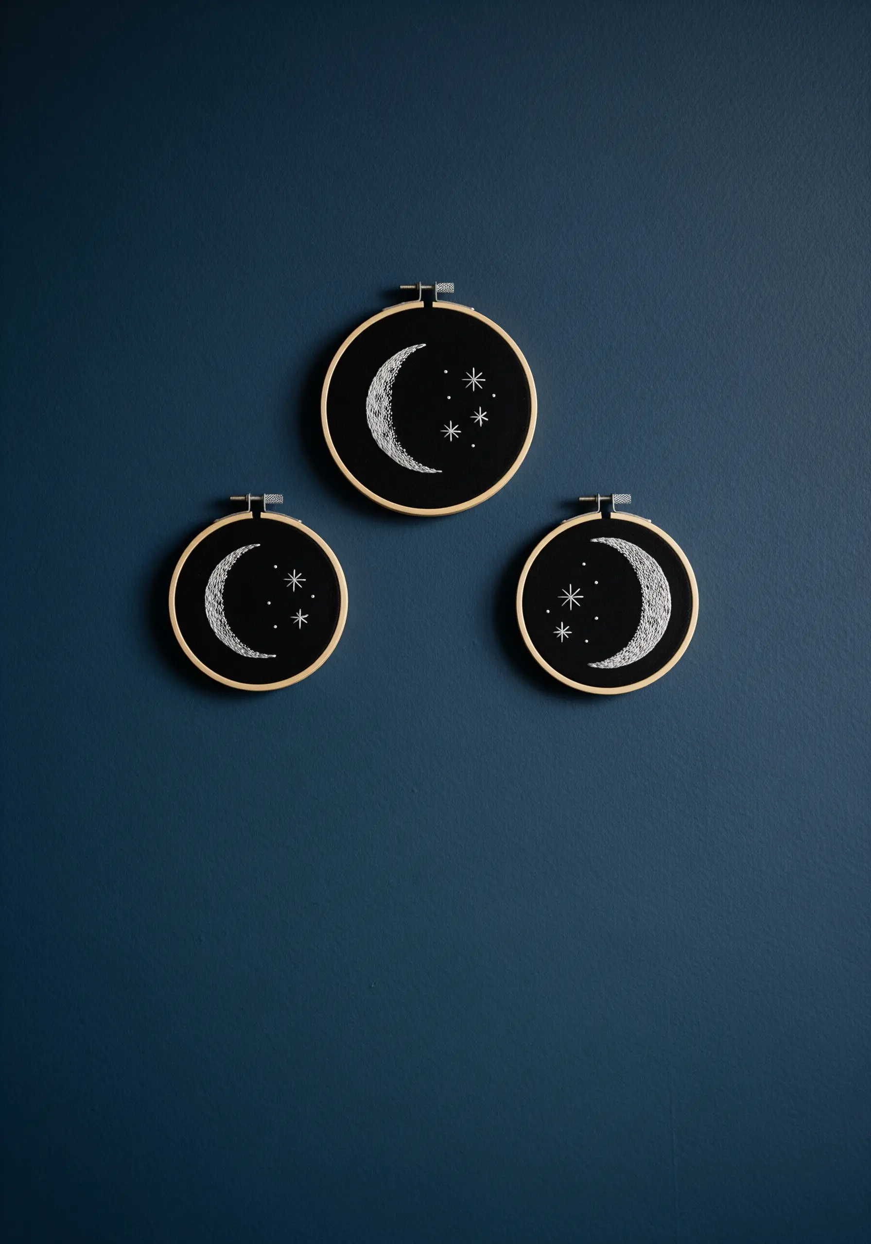 A trio of embroidered moons with textured white thread on black fabric.