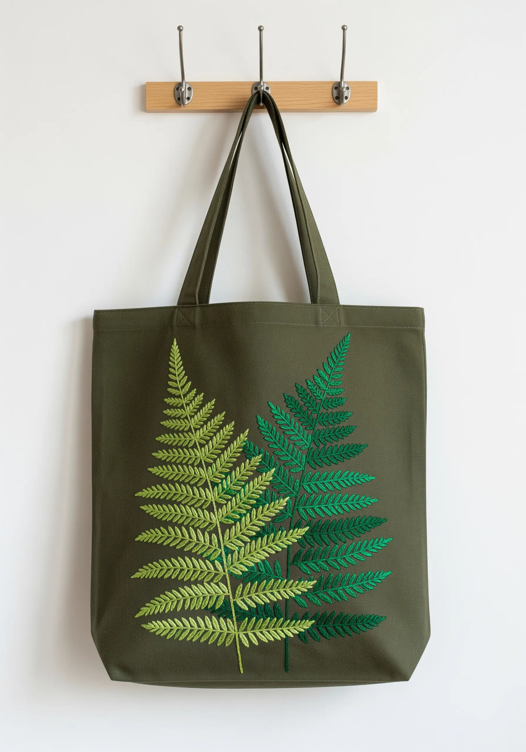 An olive green tote bag embroidered with two large fern leaves in different shades of green.