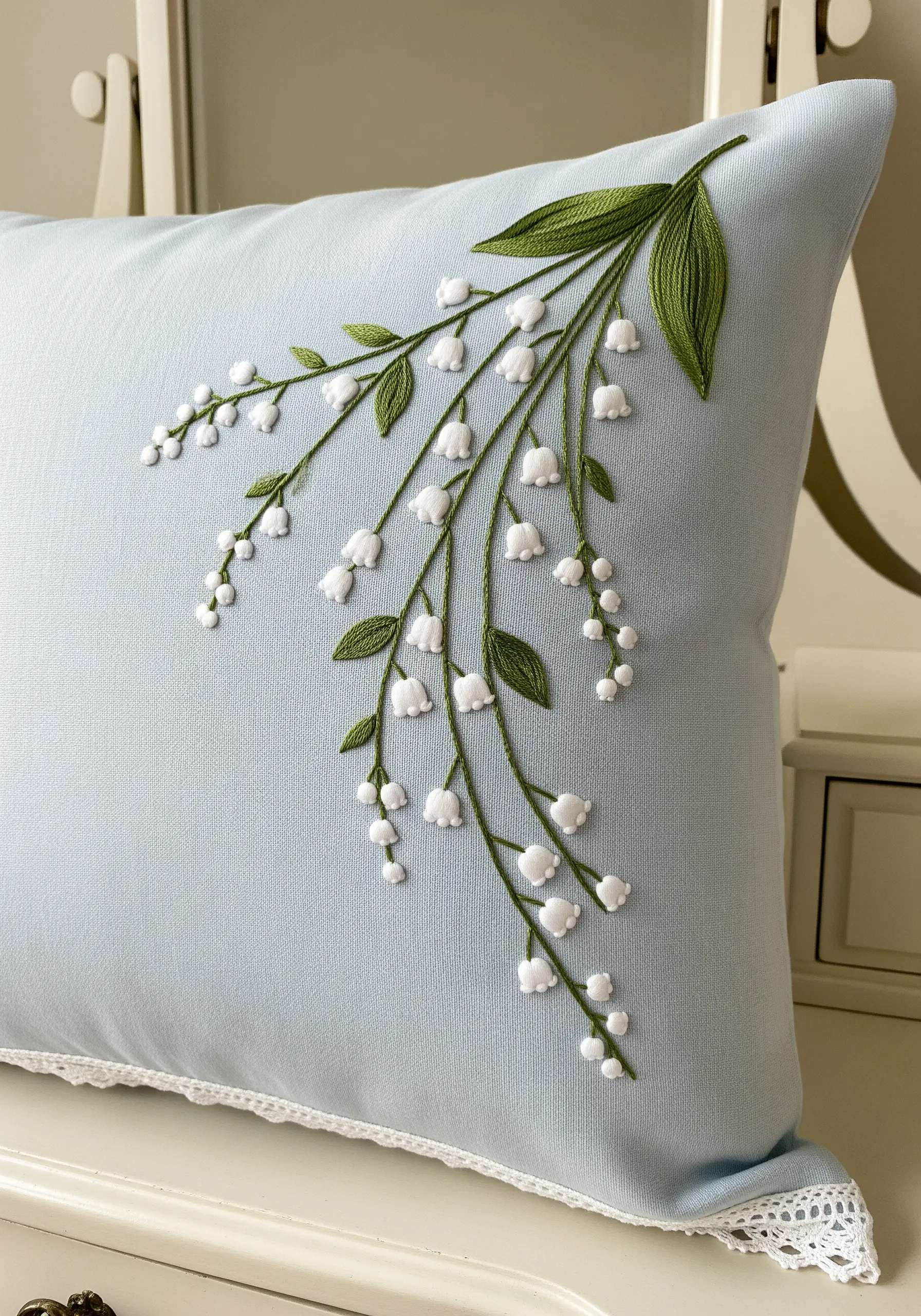 Delicate Lily of the Valley embroidery cascading down the corner of a light blue pillow.