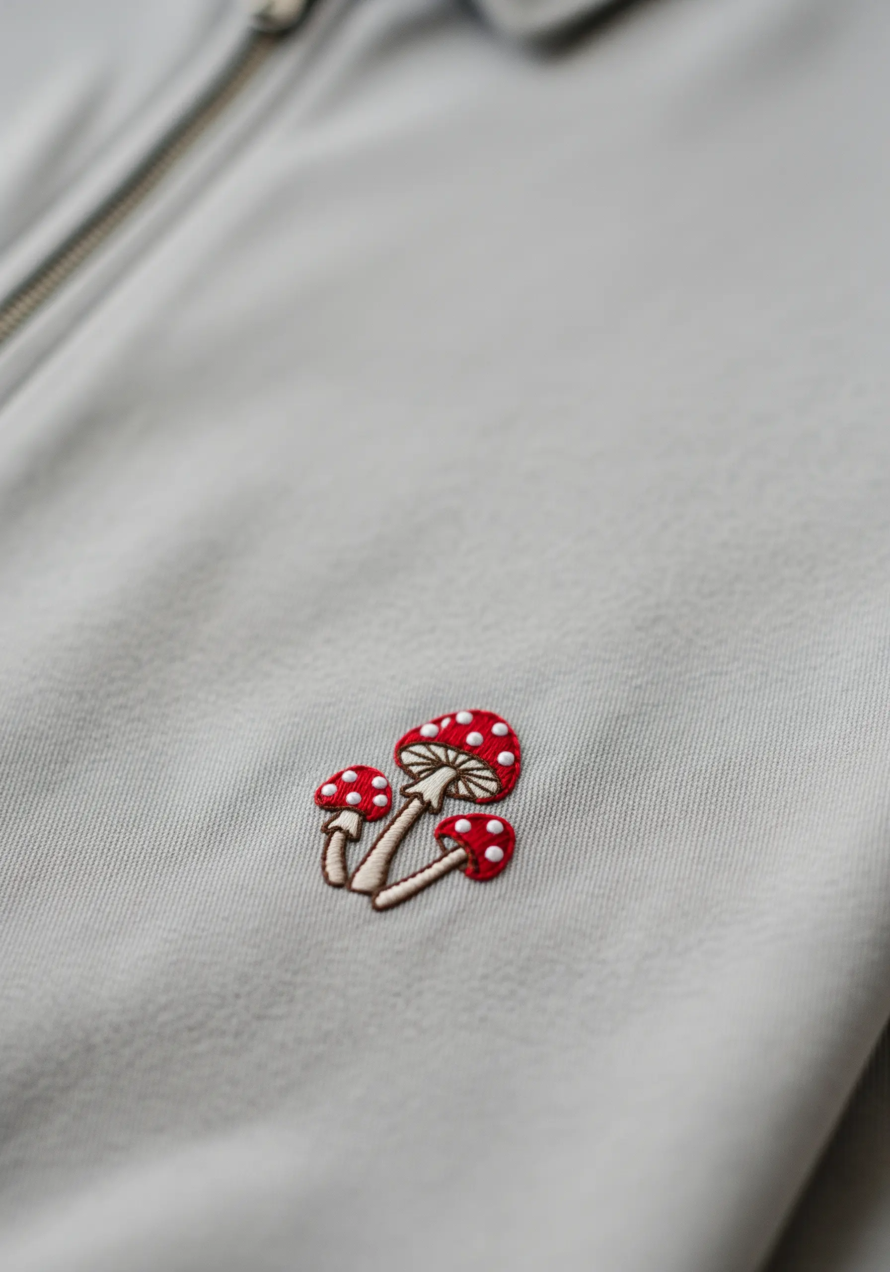 A tiny trio of red-capped mushrooms with white spots embroidered on a light gray jacket.