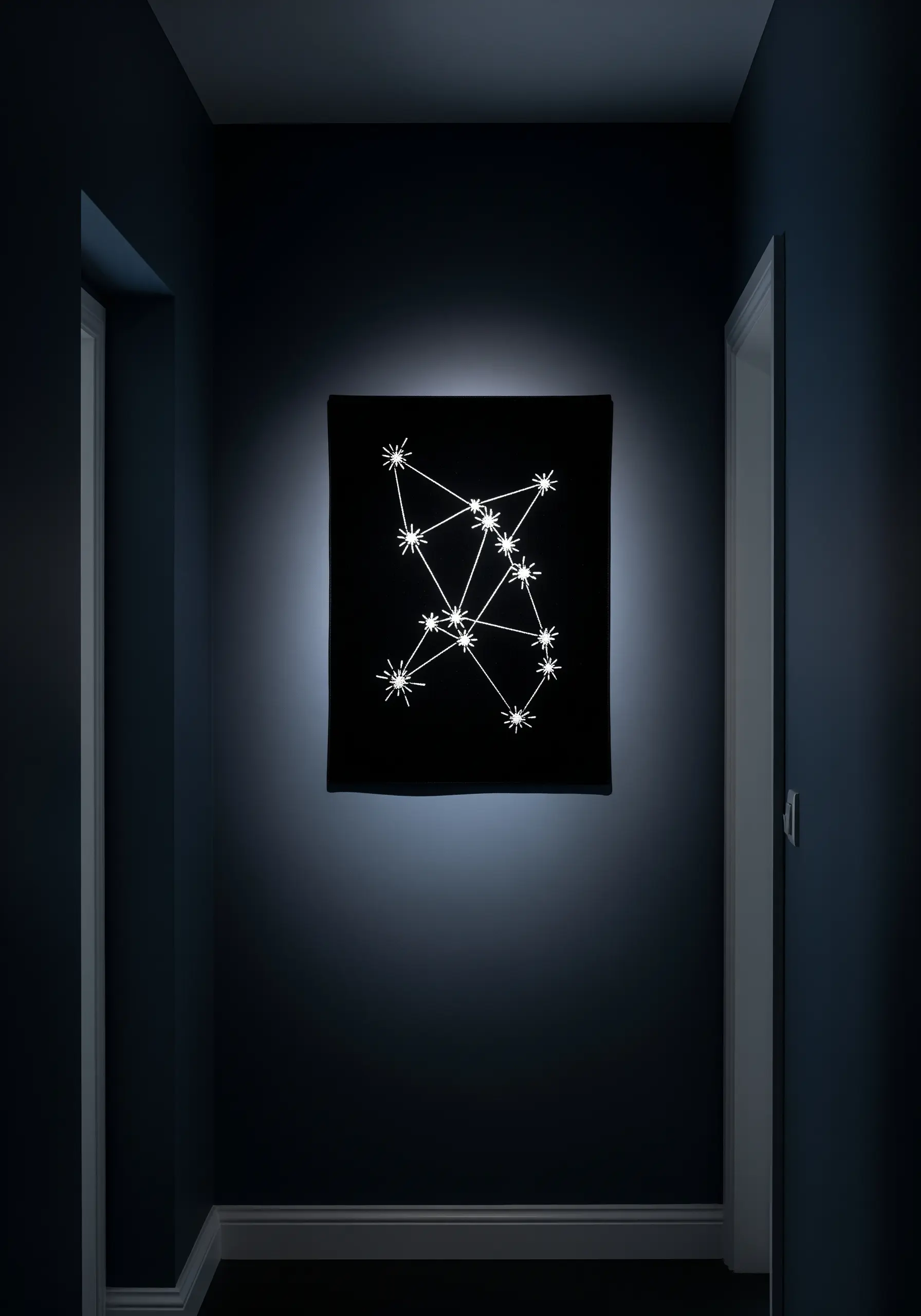 An embroidered constellation with bright white thread on a black fabric canvas, spotlit on a dark wall.