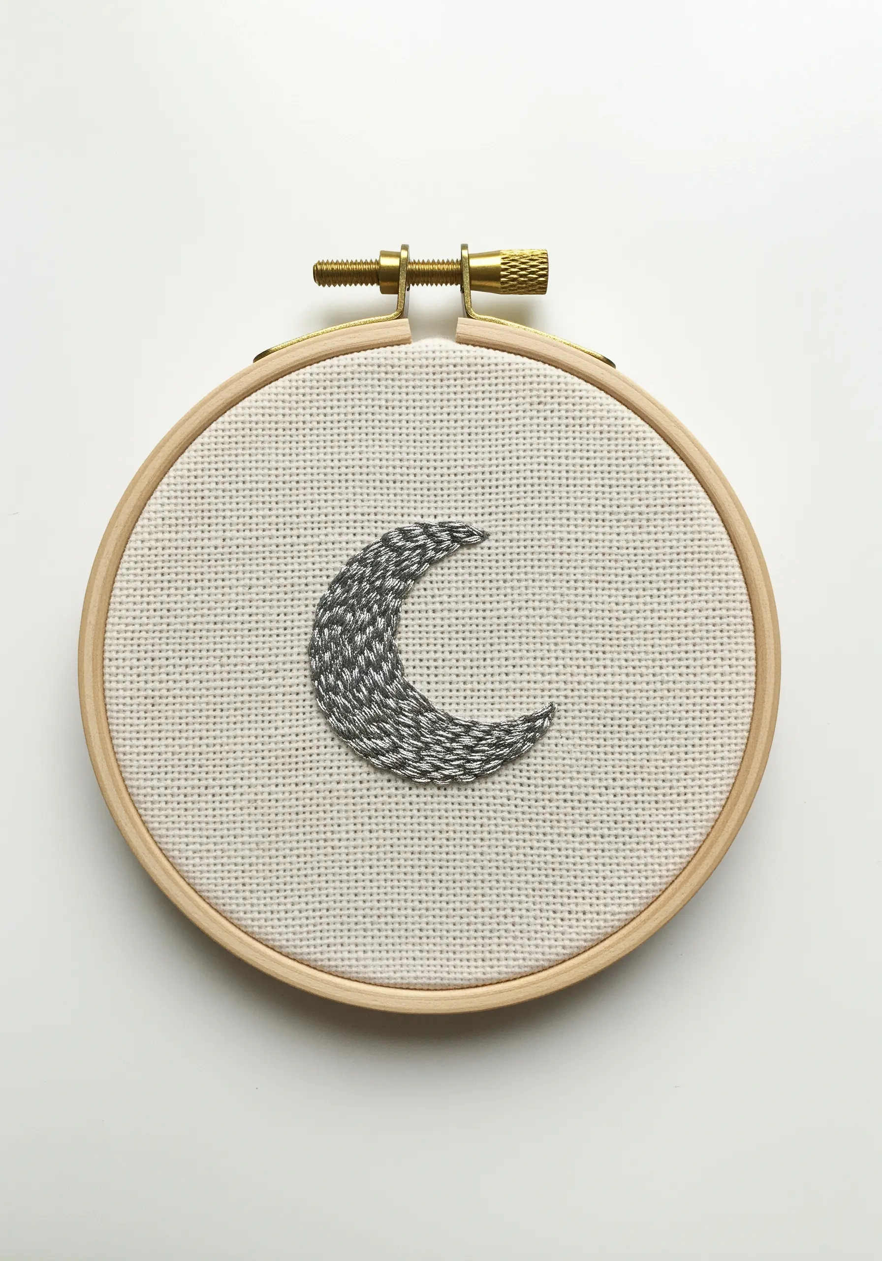 Crescent moon filled with variegated grey and white thread on Aida cloth in a hoop.