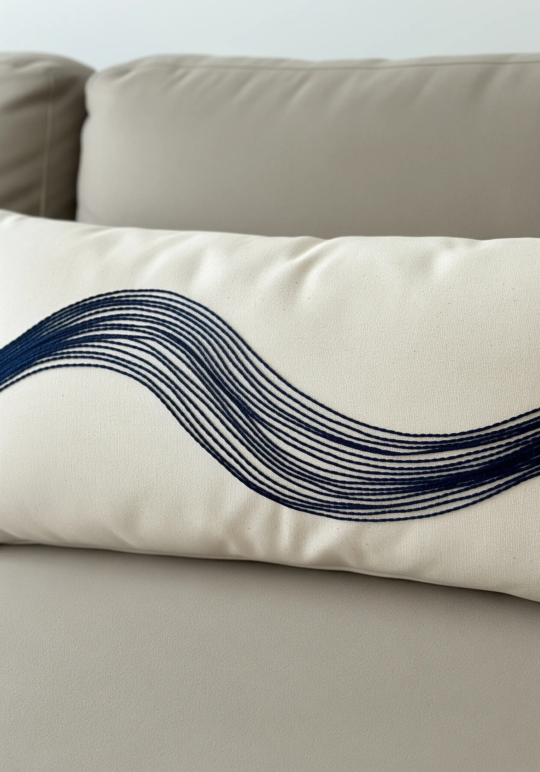 Abstract wave pattern embroidered with long, parallel dark blue threads on a white cushion.