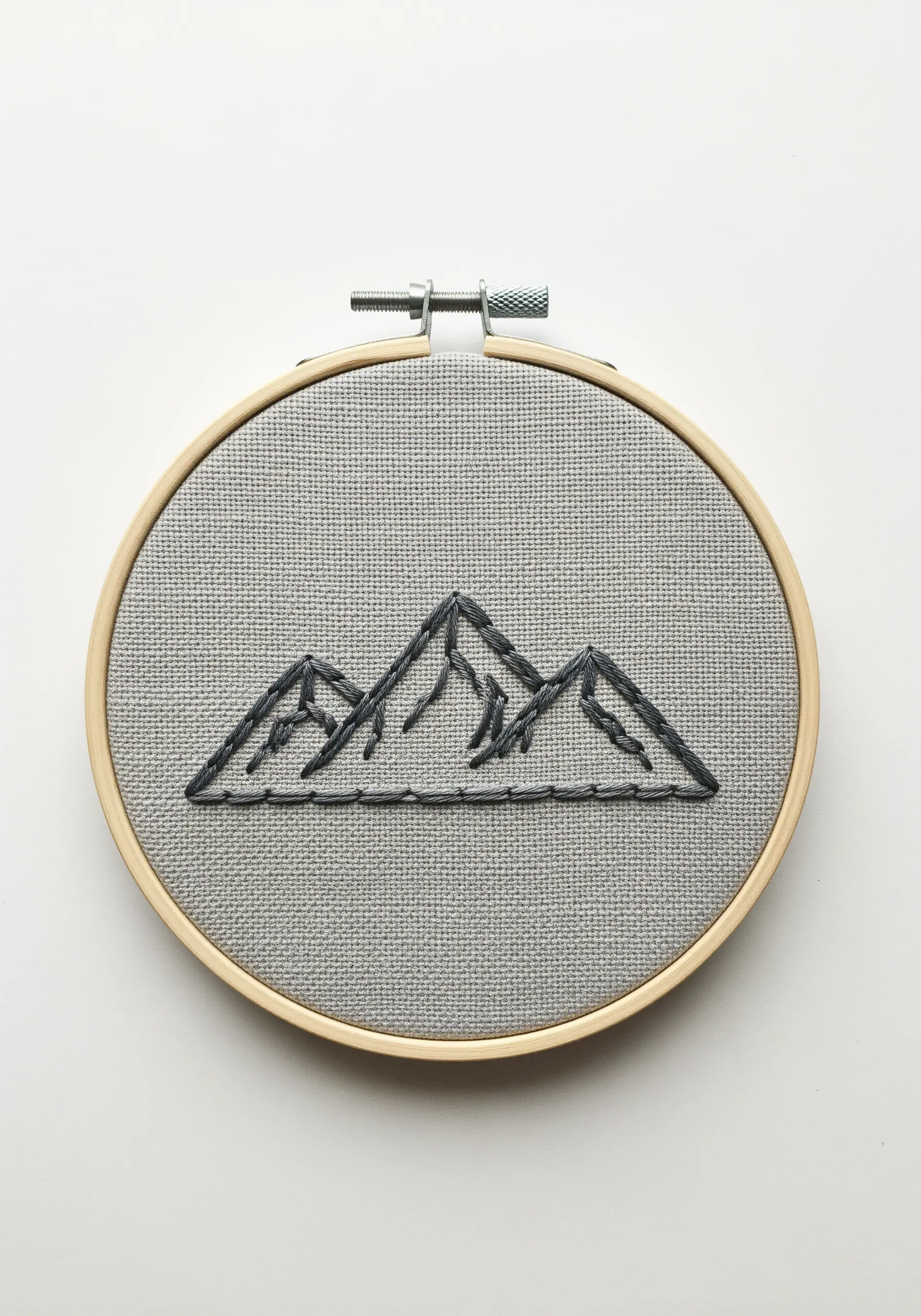 A minimalist mountain range outline stitched in dark thread on gray fabric.