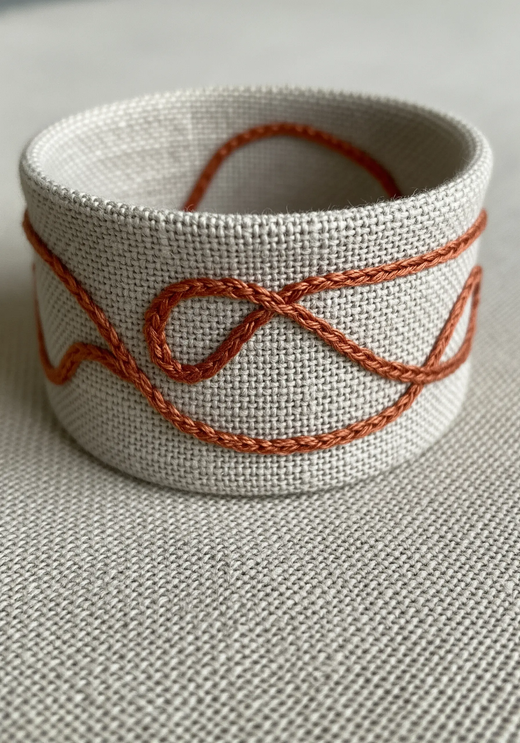An abstract, interwoven orange line using a Pekinese stitch on a fabric cuff.