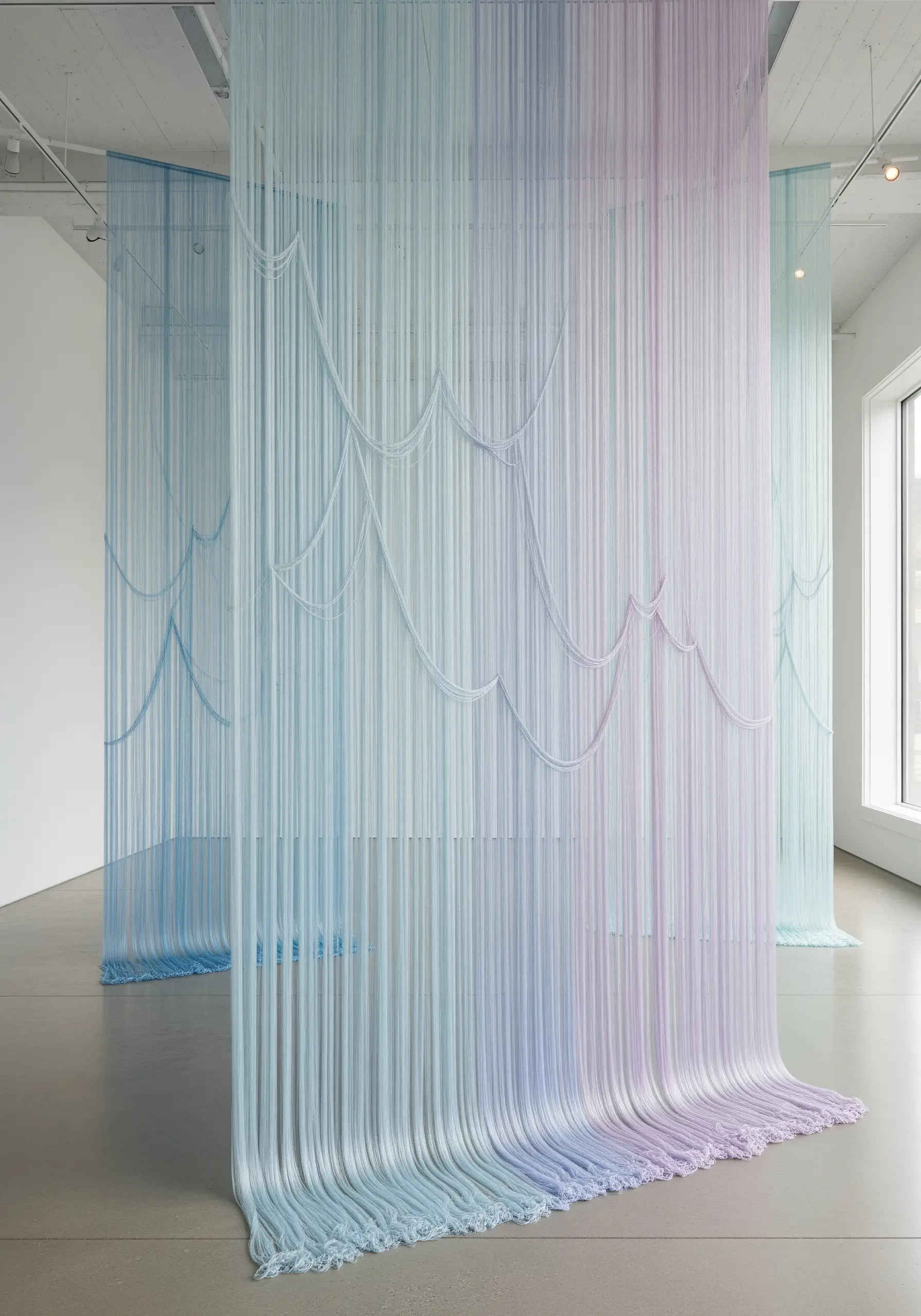 Floor-to-ceiling installation of fine threads in a pastel gradient of blue, lilac, and mint.