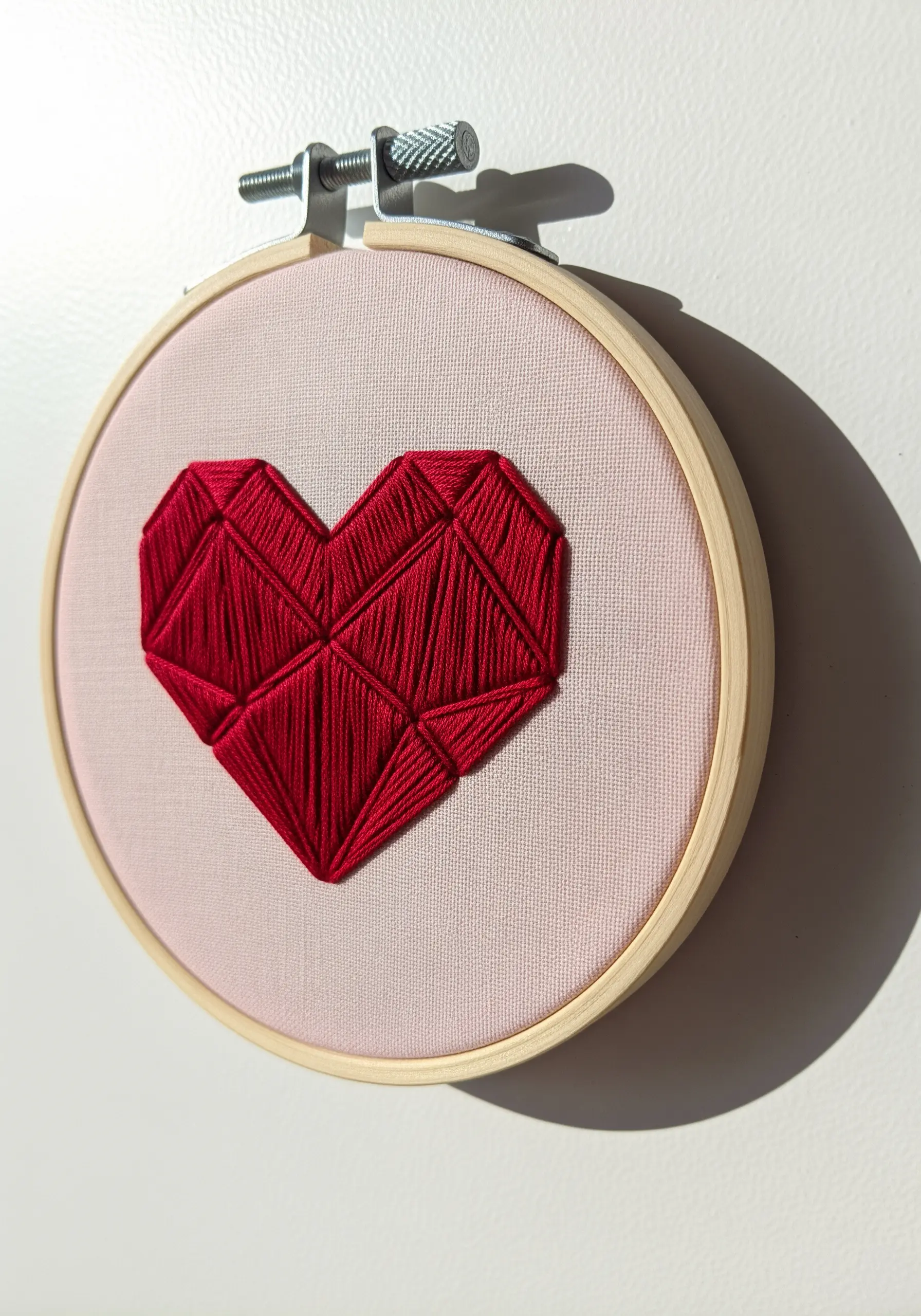 A red geometric heart filled with satin stitches in varying directions.