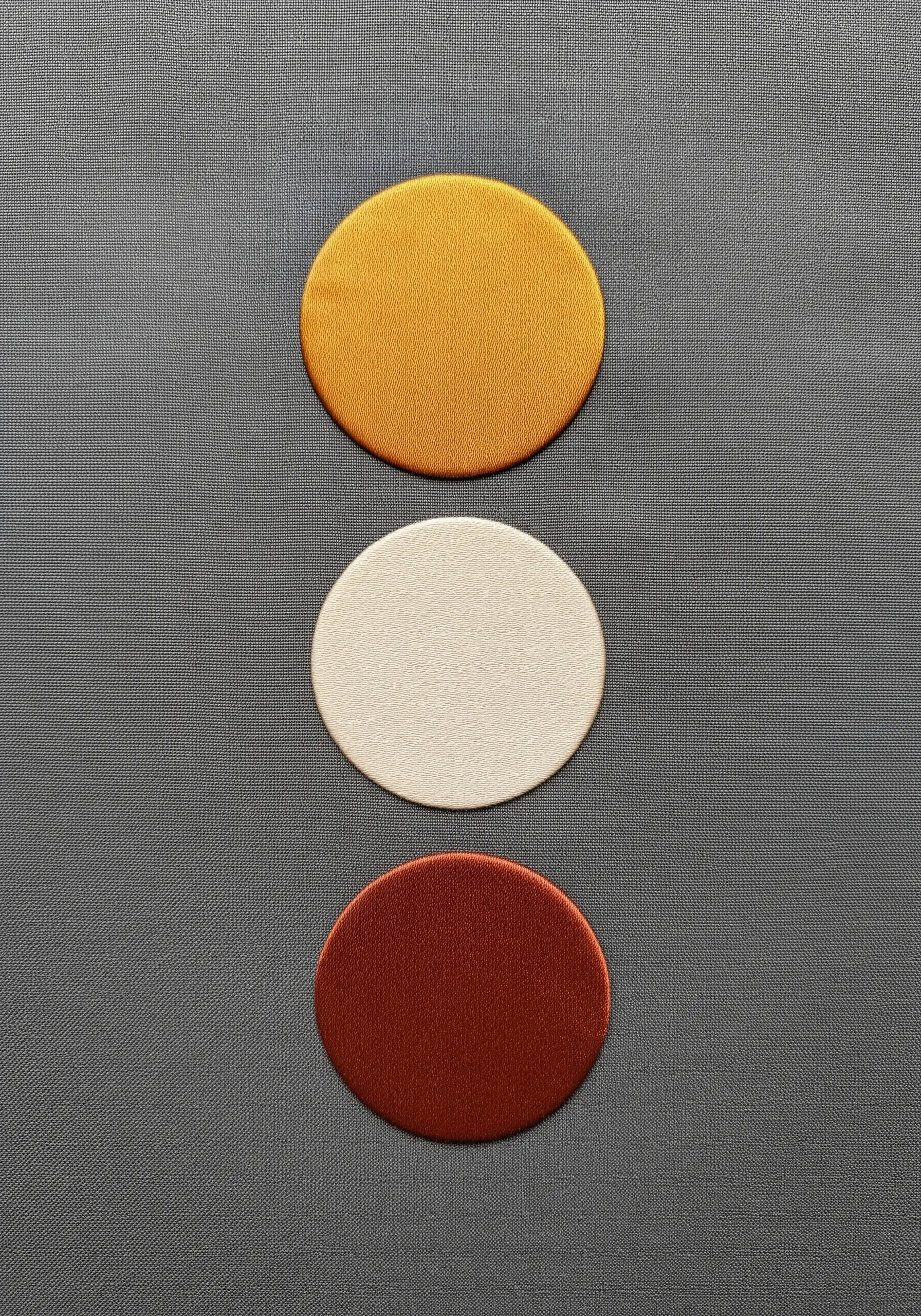 Three perfectly satin-stitched circles in yellow, cream, and brick red on grey fabric.