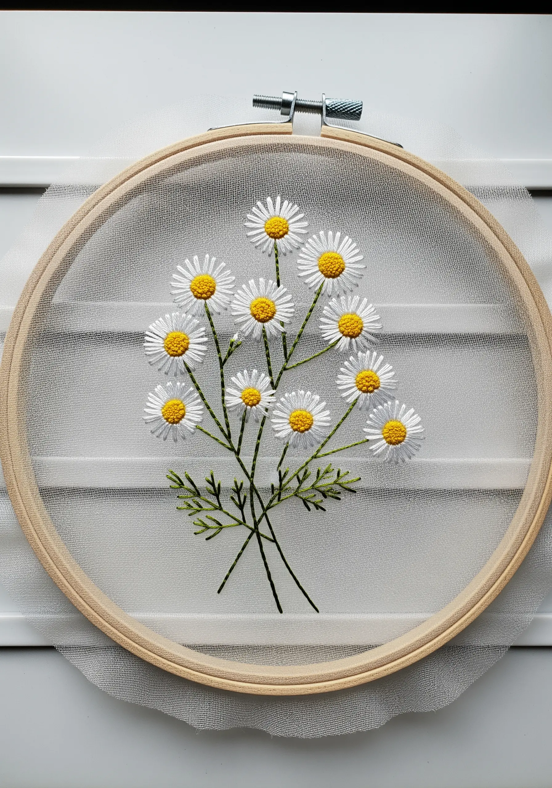 A bouquet of chamomile flowers with white petals embroidered on transparent tulle fabric in a hoop.