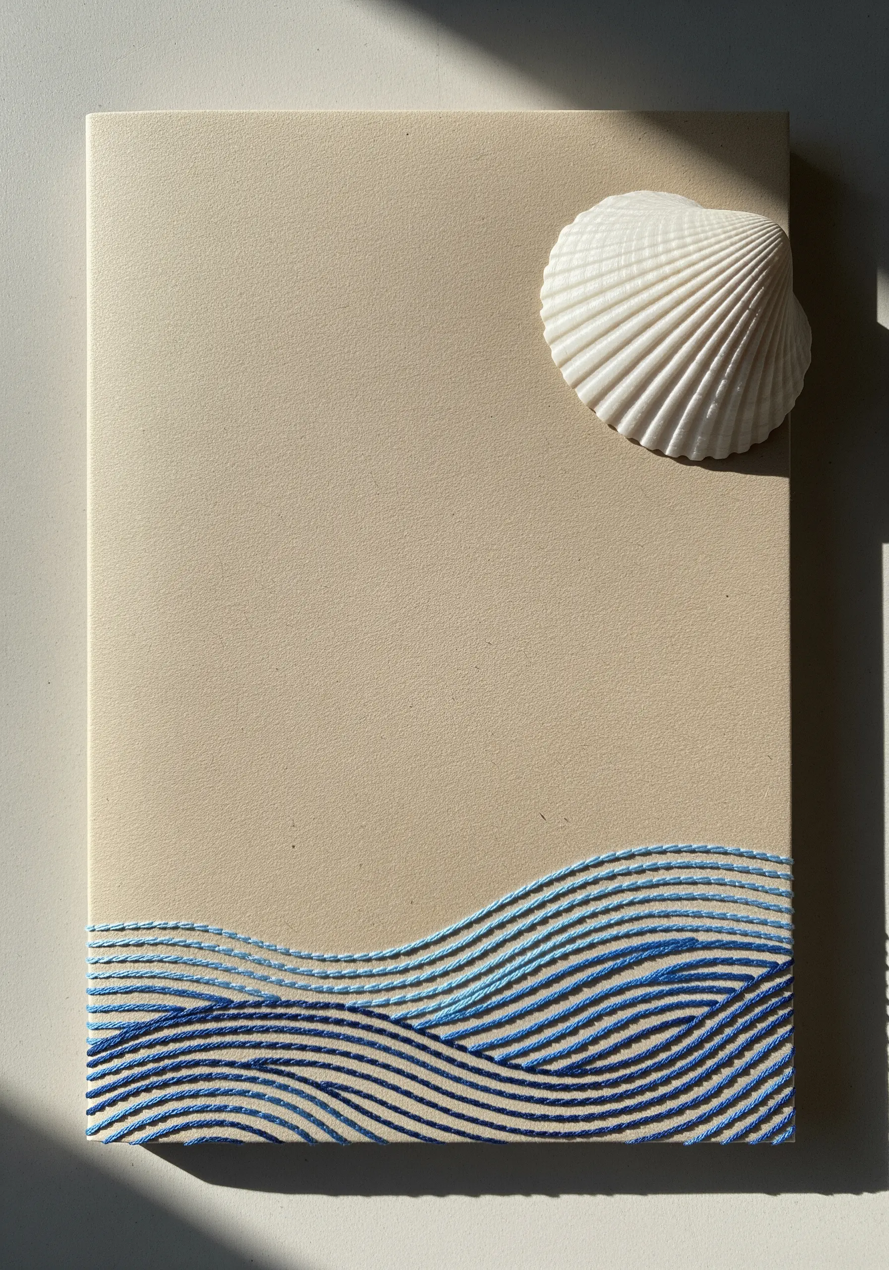 Embroidered ocean waves in varying shades of blue on a sand-colored notebook.