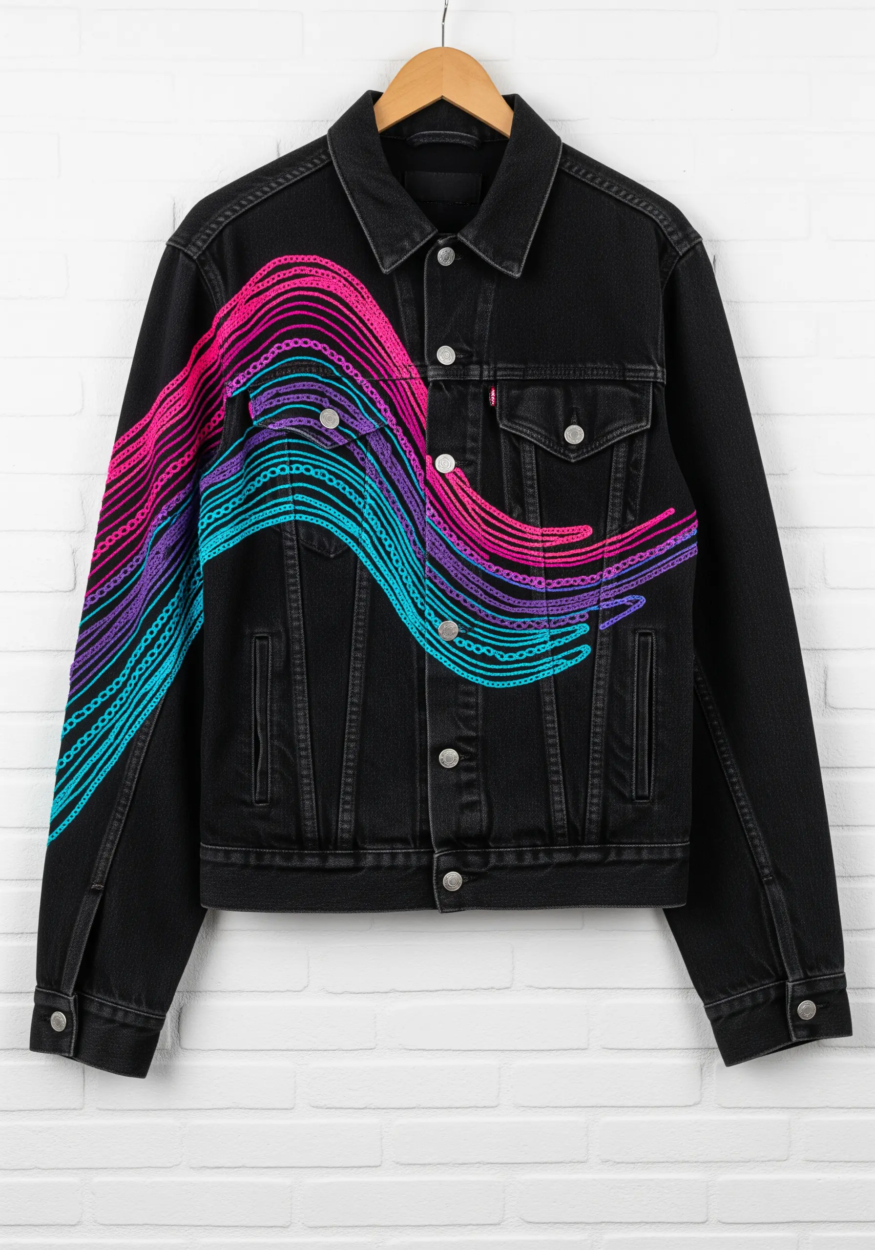 Flowing waves of neon pink, blue, and purple chain stitch across a black denim jacket.