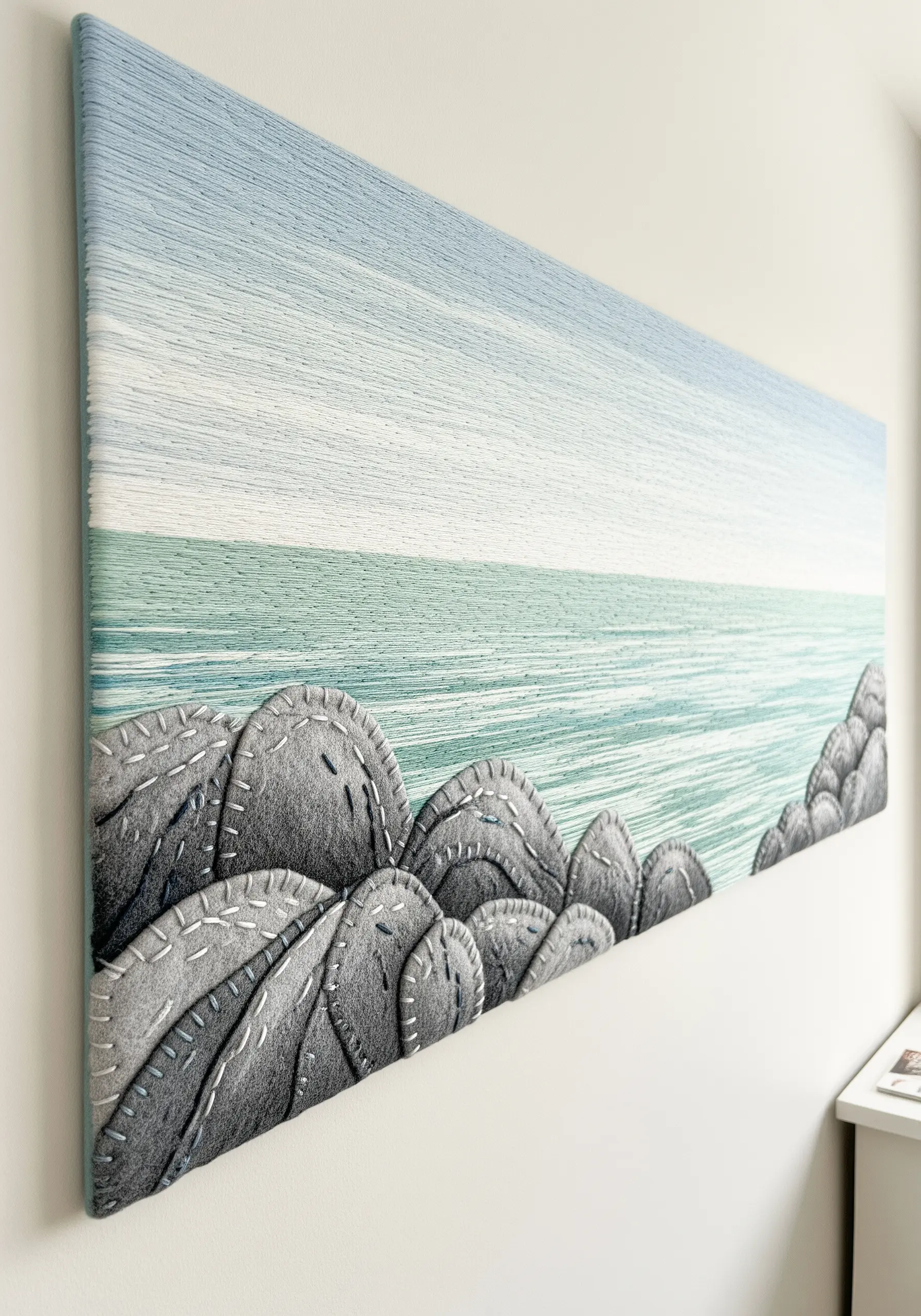 Embroidered coastal scene on canvas with gray felt appliqué rocks in the foreground.