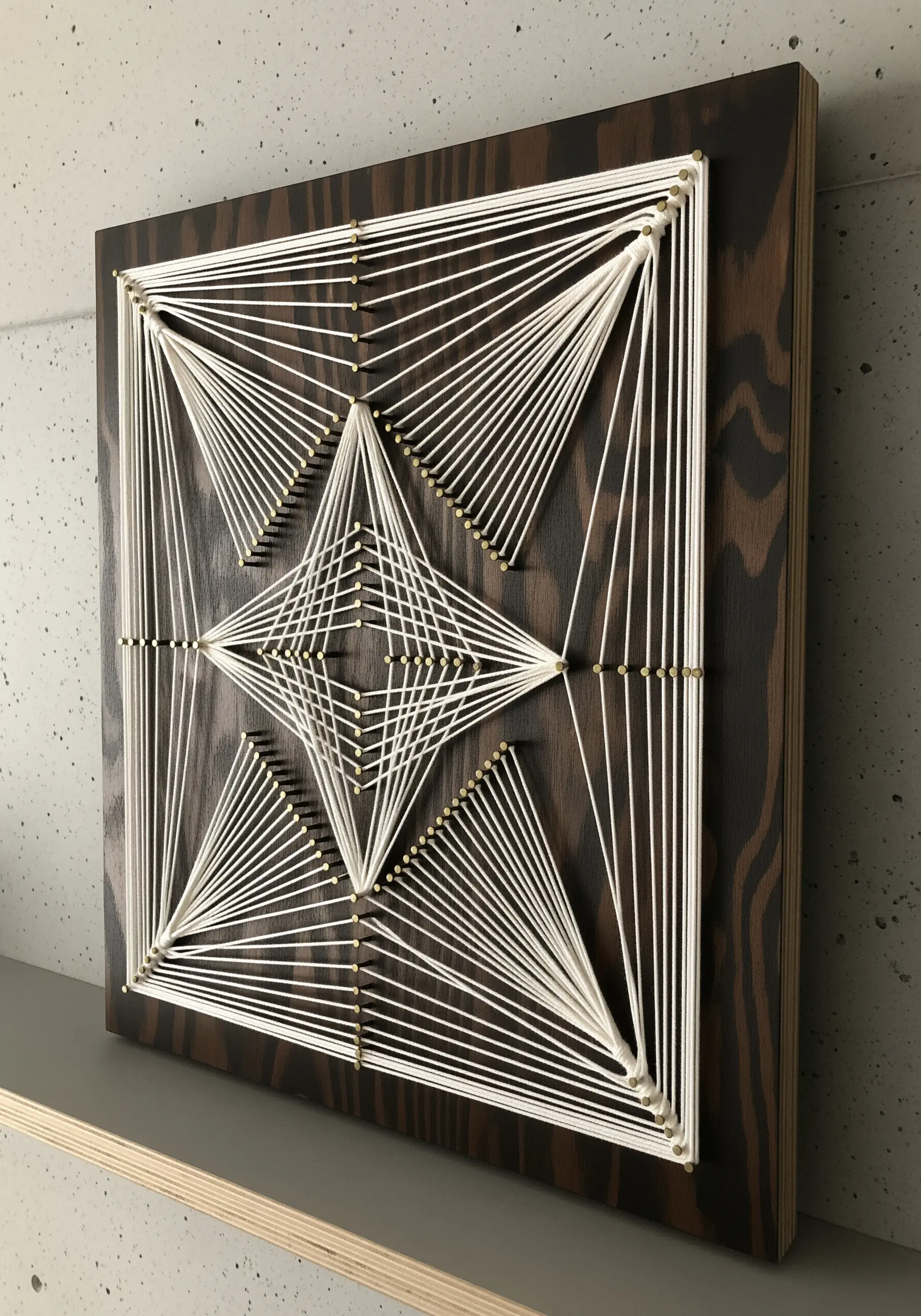 Geometric string art with white thread on a dark wooden board, creating star-like patterns.