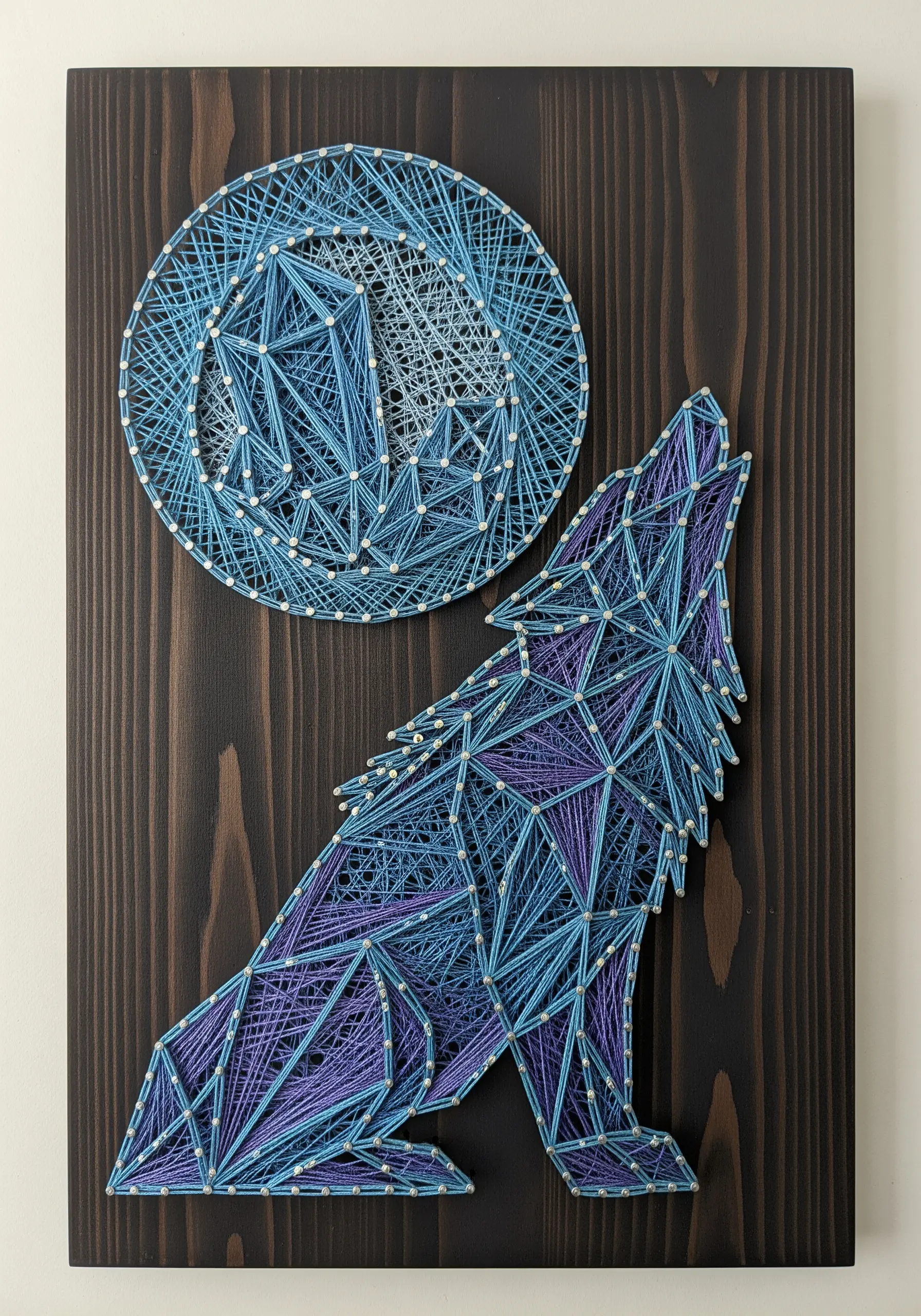Geometric string art of a howling wolf and moon using blue and purple threads.