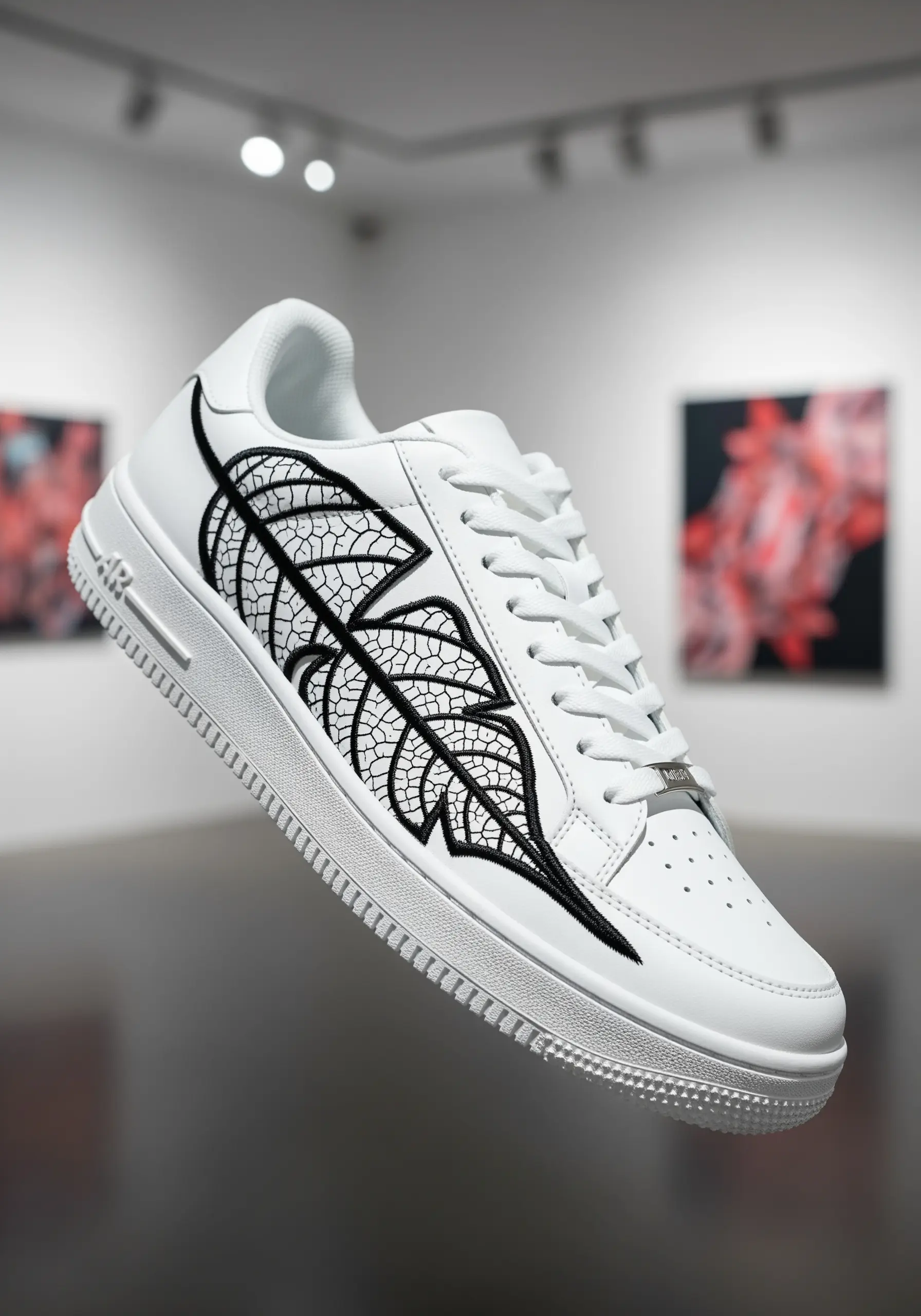 A black line-art embroidery of a skeletal leaf on the side of a white leather sneaker.