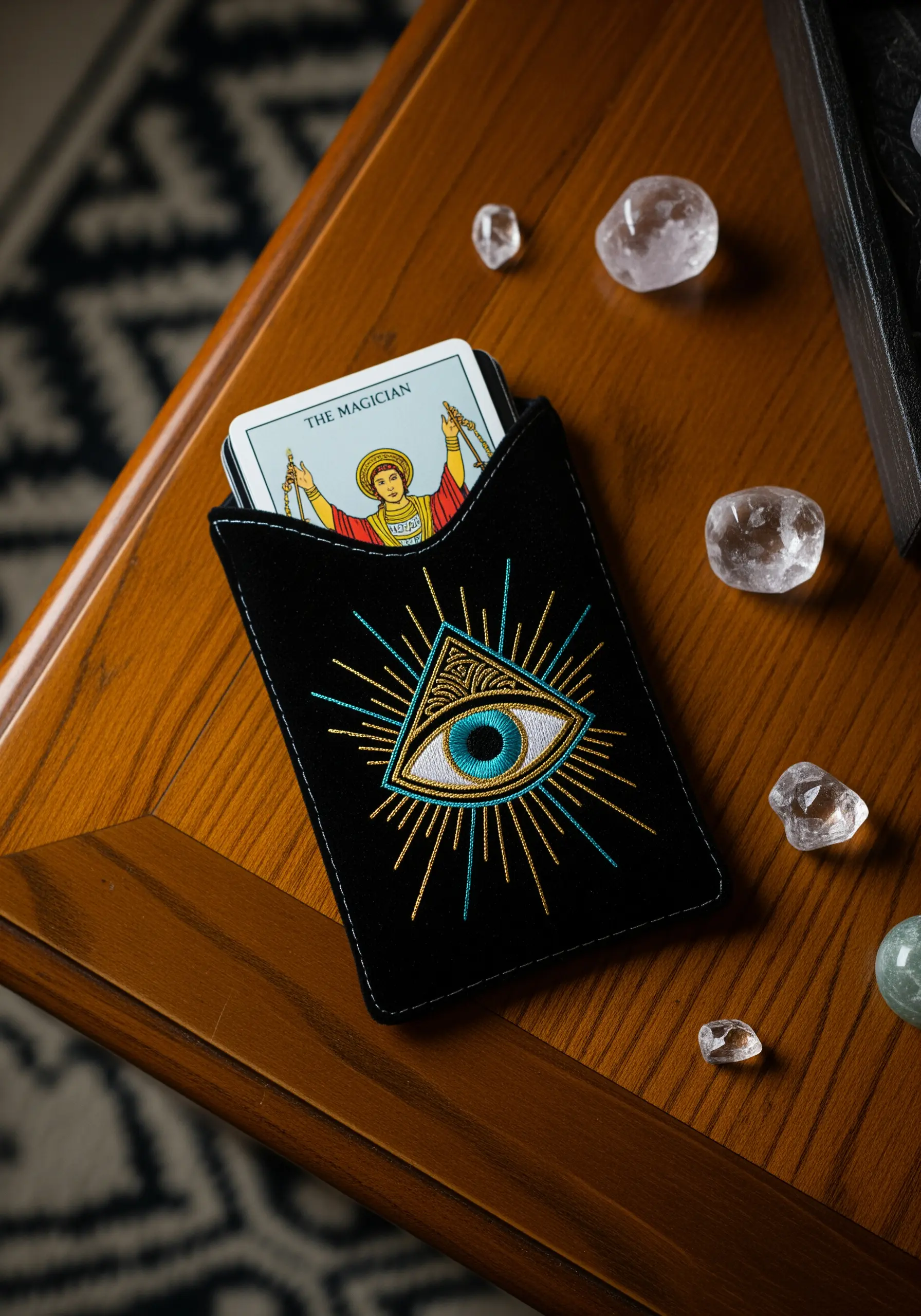 A black velvet pouch embroidered with a gold and teal all-seeing eye tarot design.