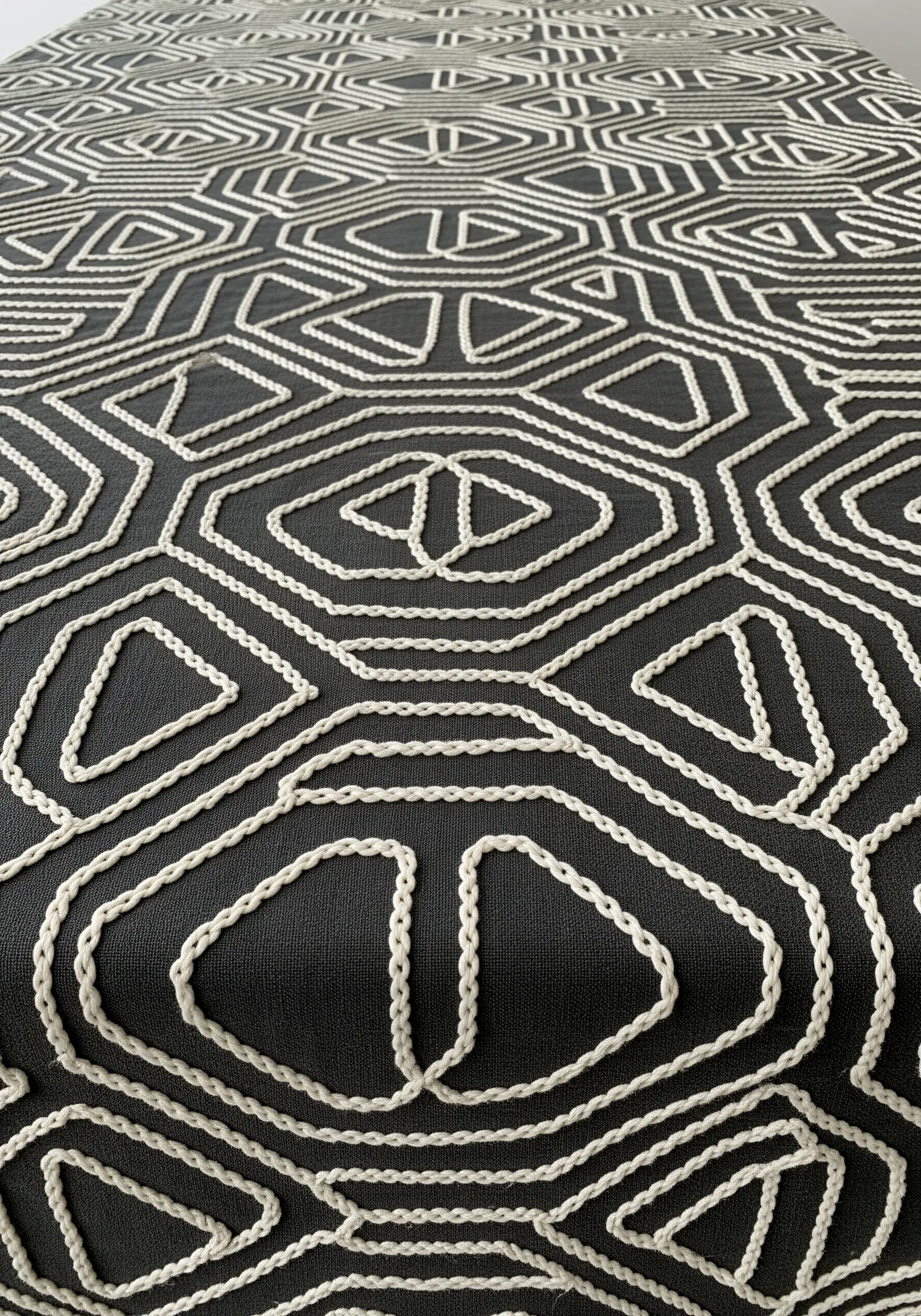 A close-up of a black tablecloth with a bold geometric pattern made from thick, couched white cord.