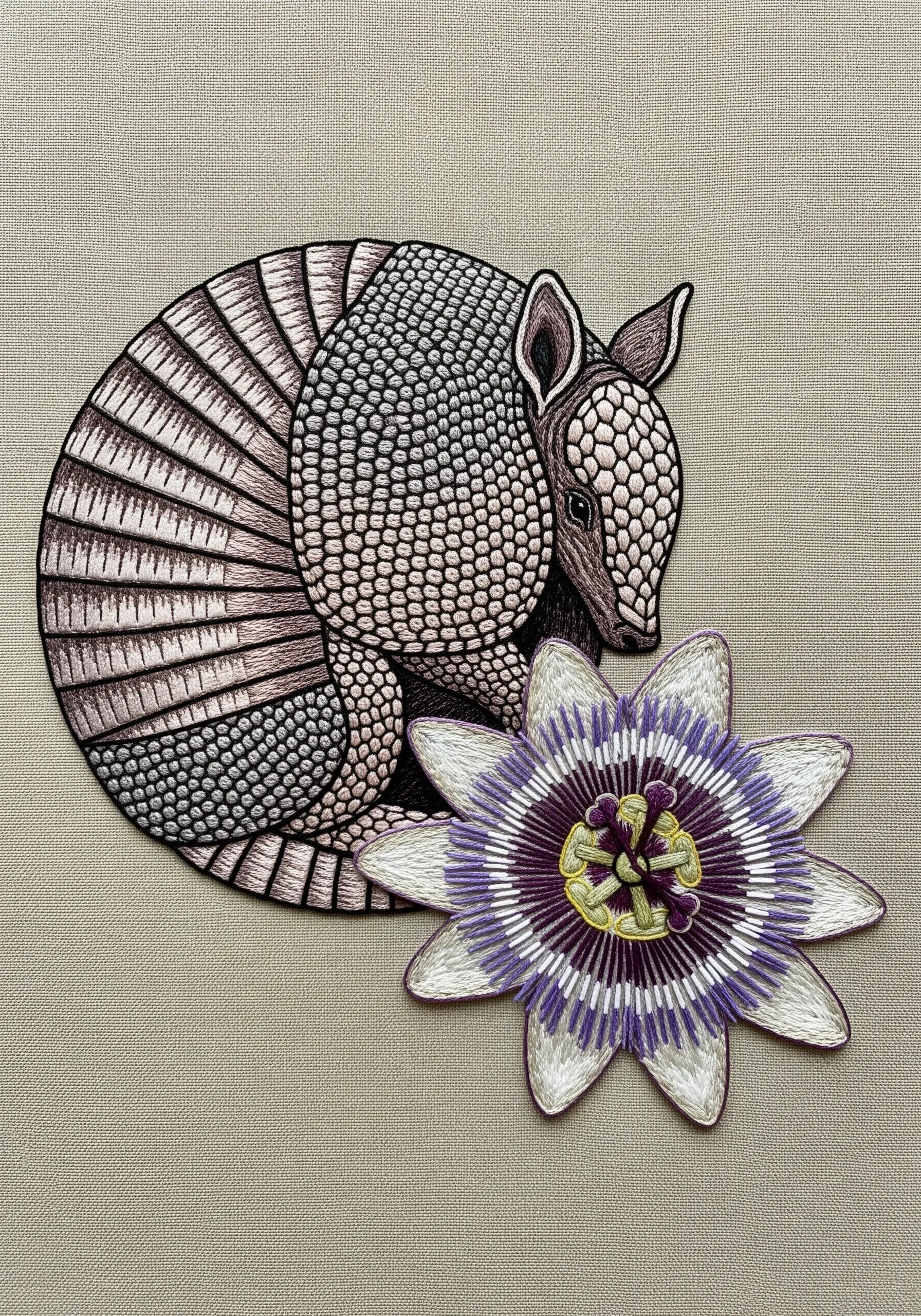 A detailed embroidery of a curled-up armadillo, with its shell textured by tiny stitches.