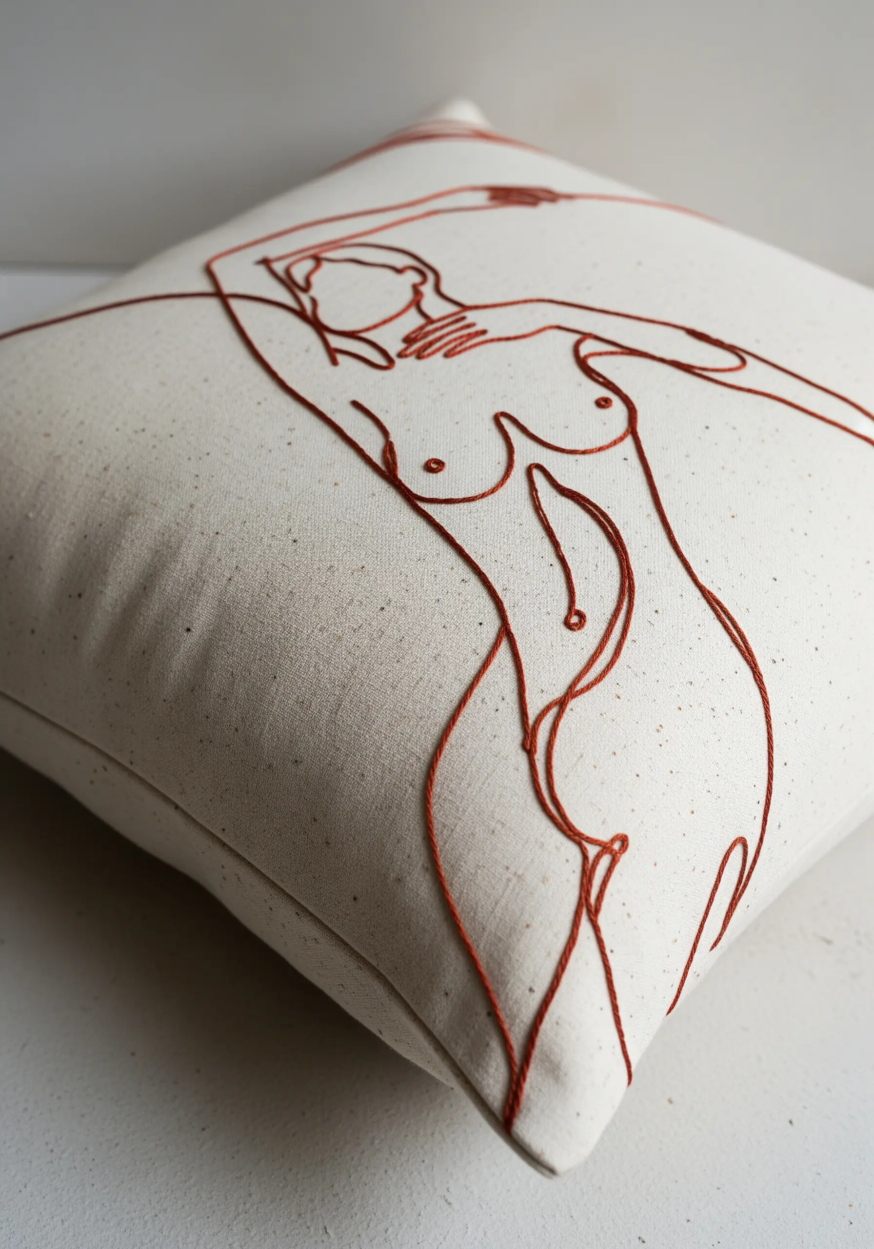 Abstract line art of a female figure, stitched in warm brown thread on a cream cushion.