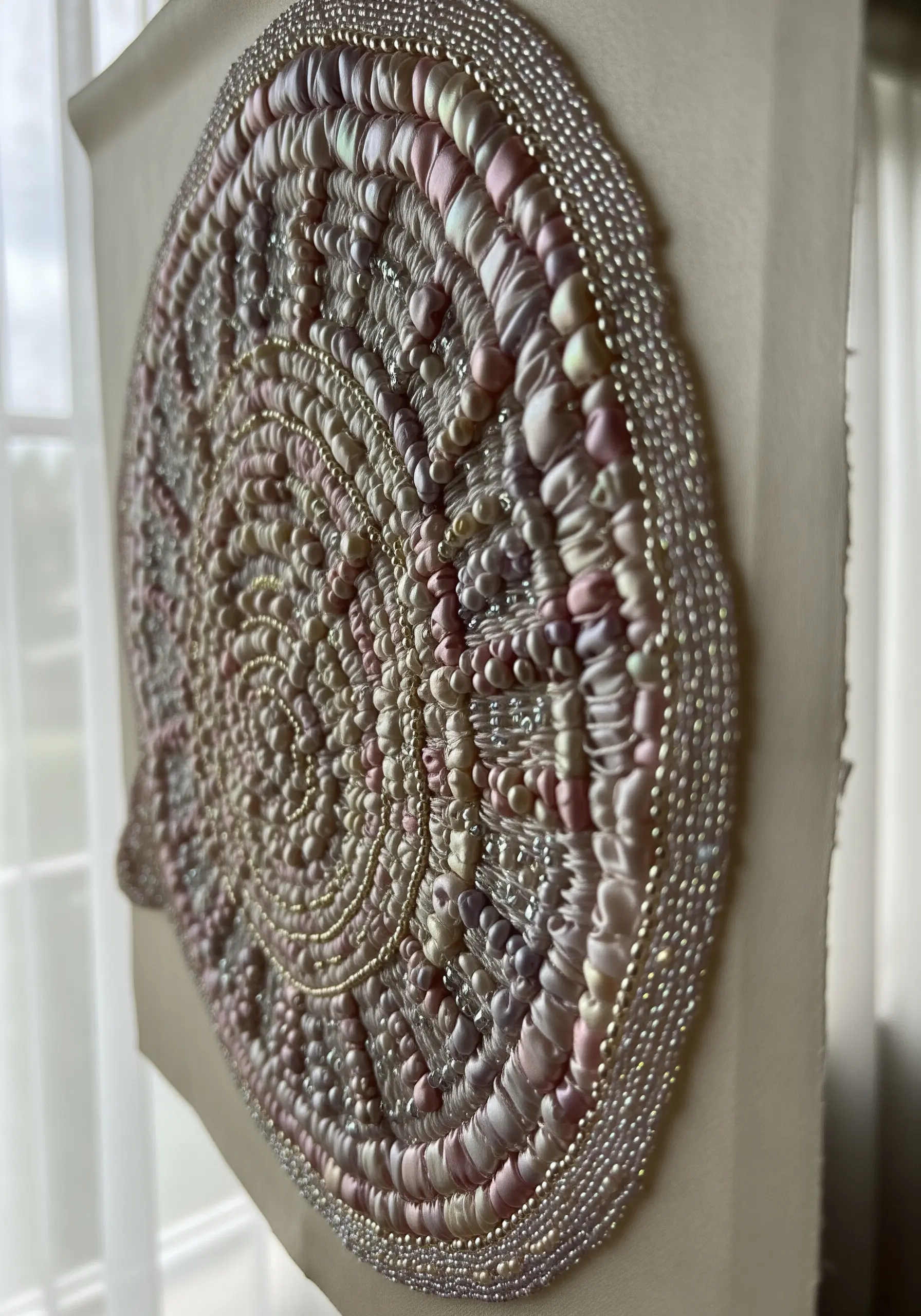 Close-up of a circular embroidery with pink and cream silk ribbon, pearls, and iridescent beads.