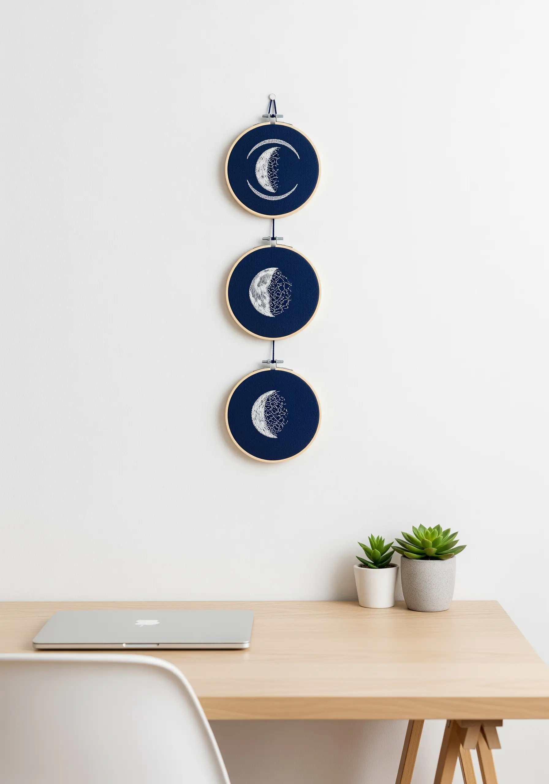A triptych of three small embroidery hoops showing phases of the moon on a dark blue background.