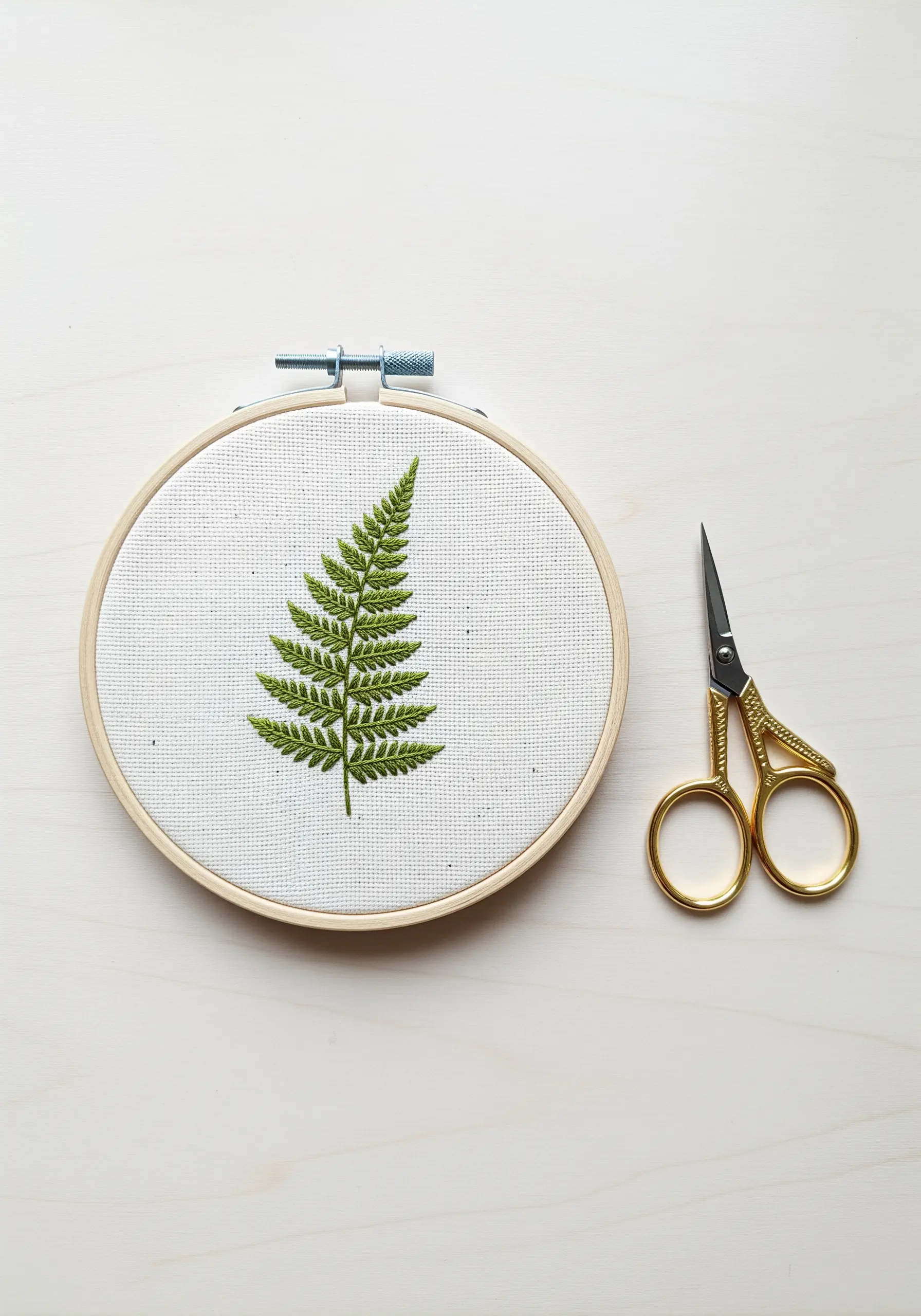 A detailed fern frond embroidered in green on white Aida cloth.