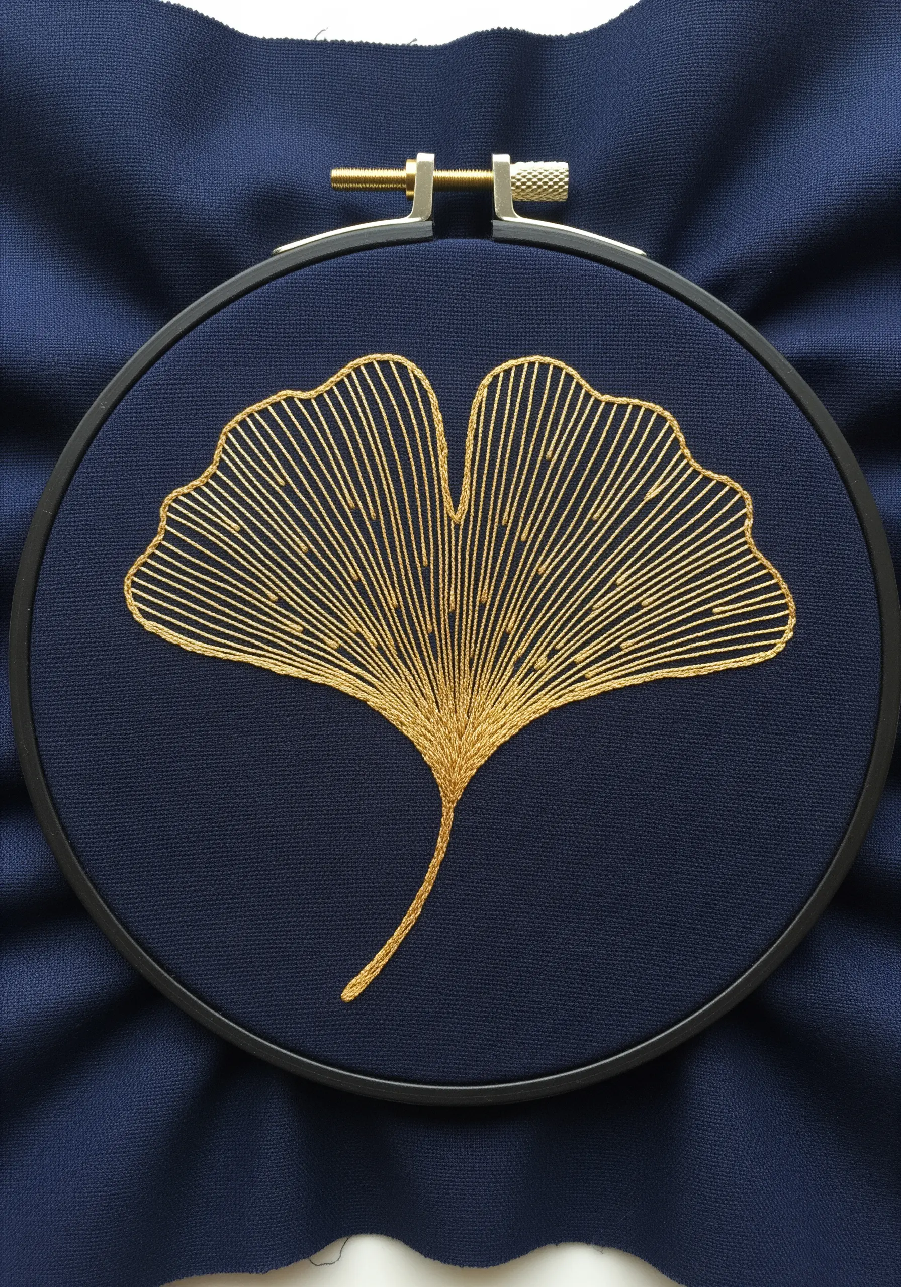 A ginkgo leaf rendered in golden metallic thread line art on dark navy fabric