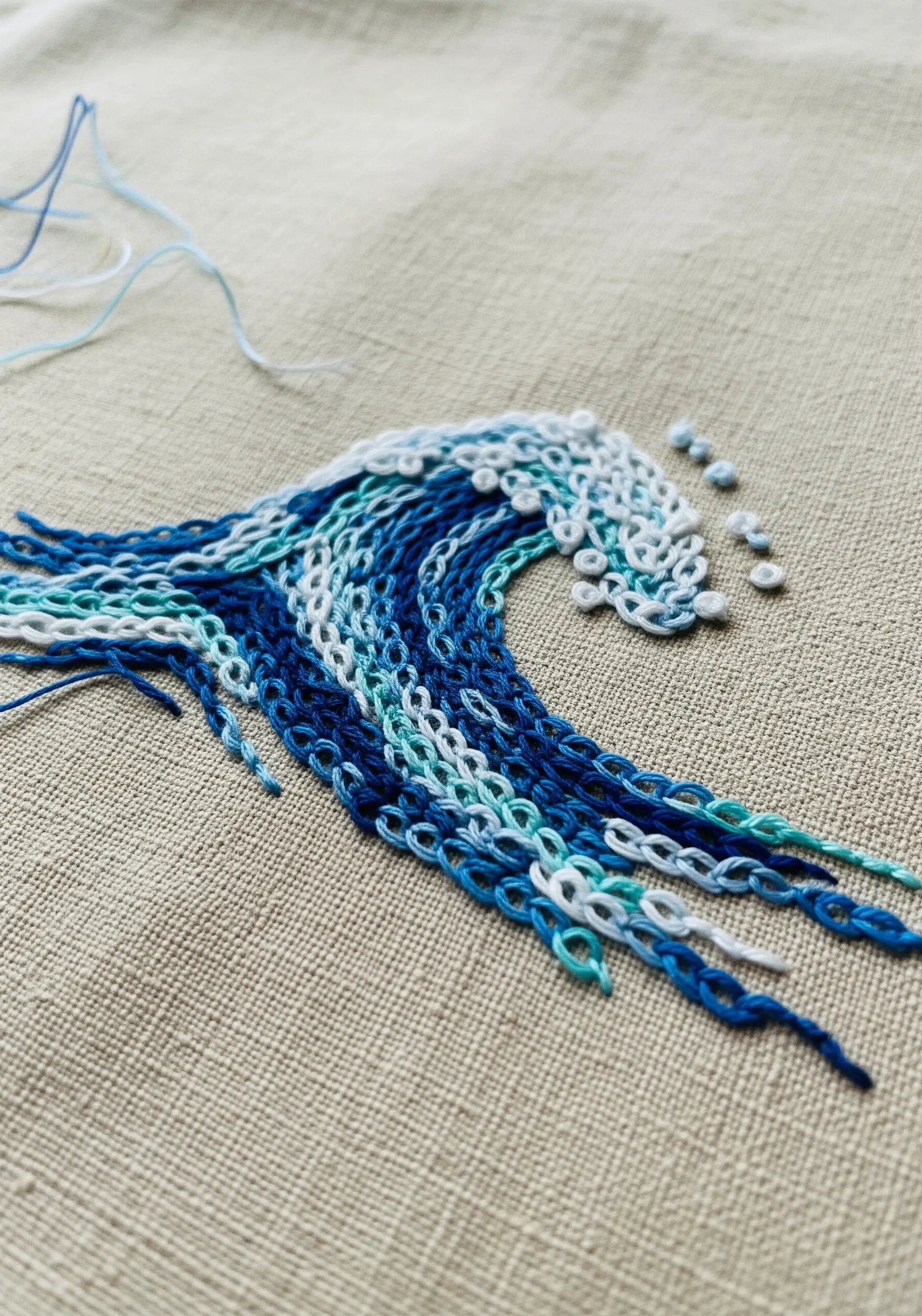 An abstract ocean wave with directional chain stitches and loose thread ends.