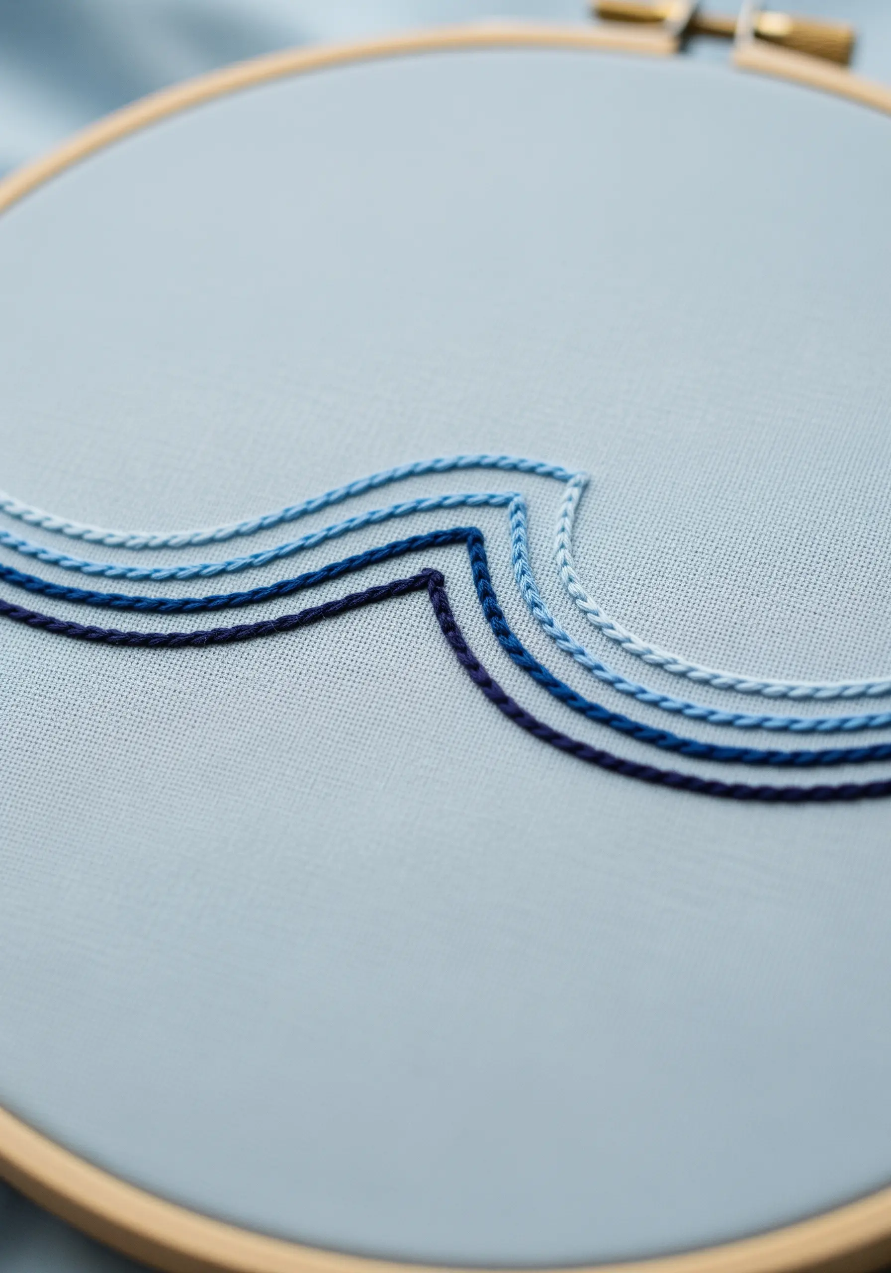 Abstract waves embroidered in a gradient of four blue shades on light blue fabric.