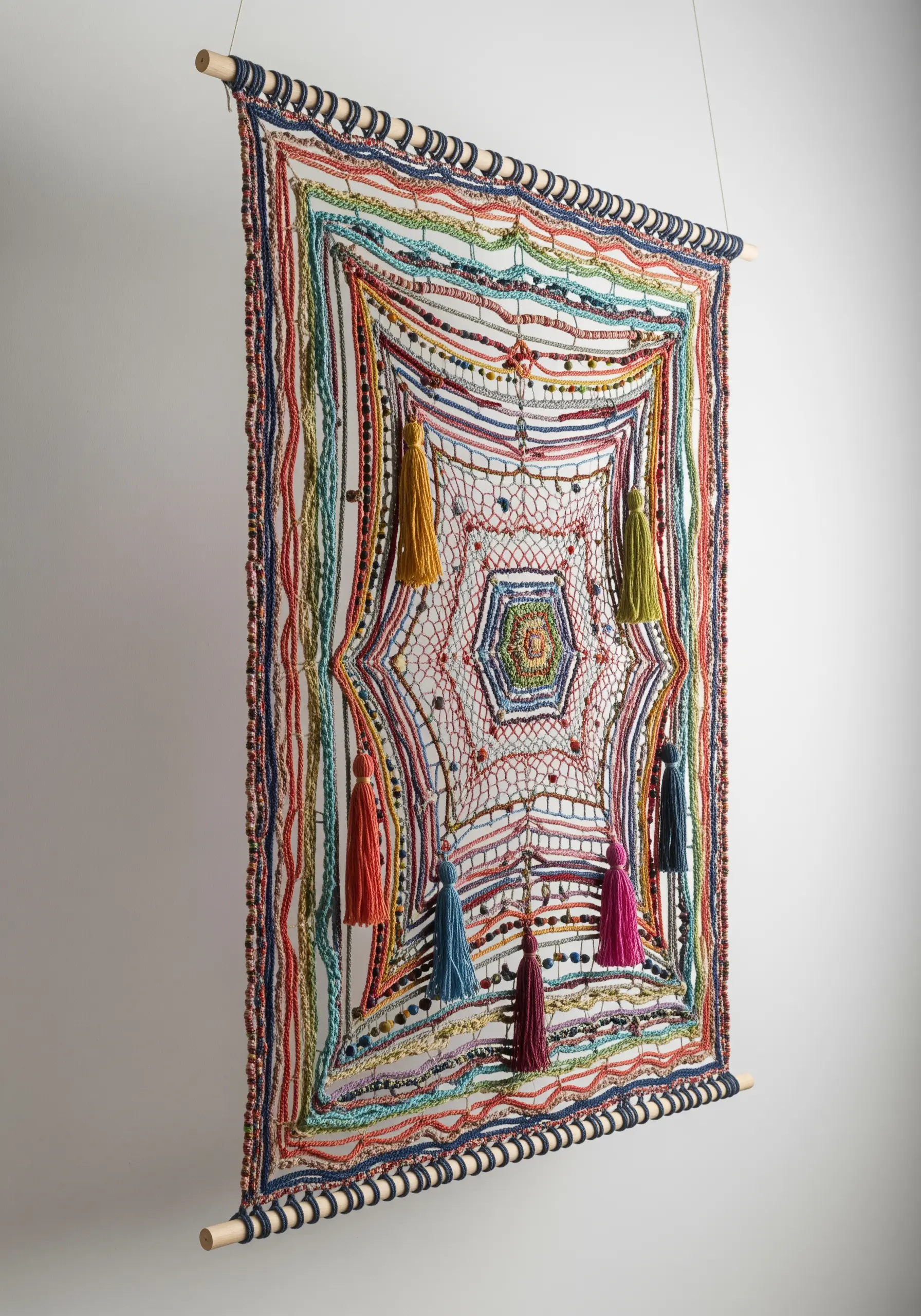 A colorful, large-scale embroidered wall hanging with open netting, beads, and tassels
