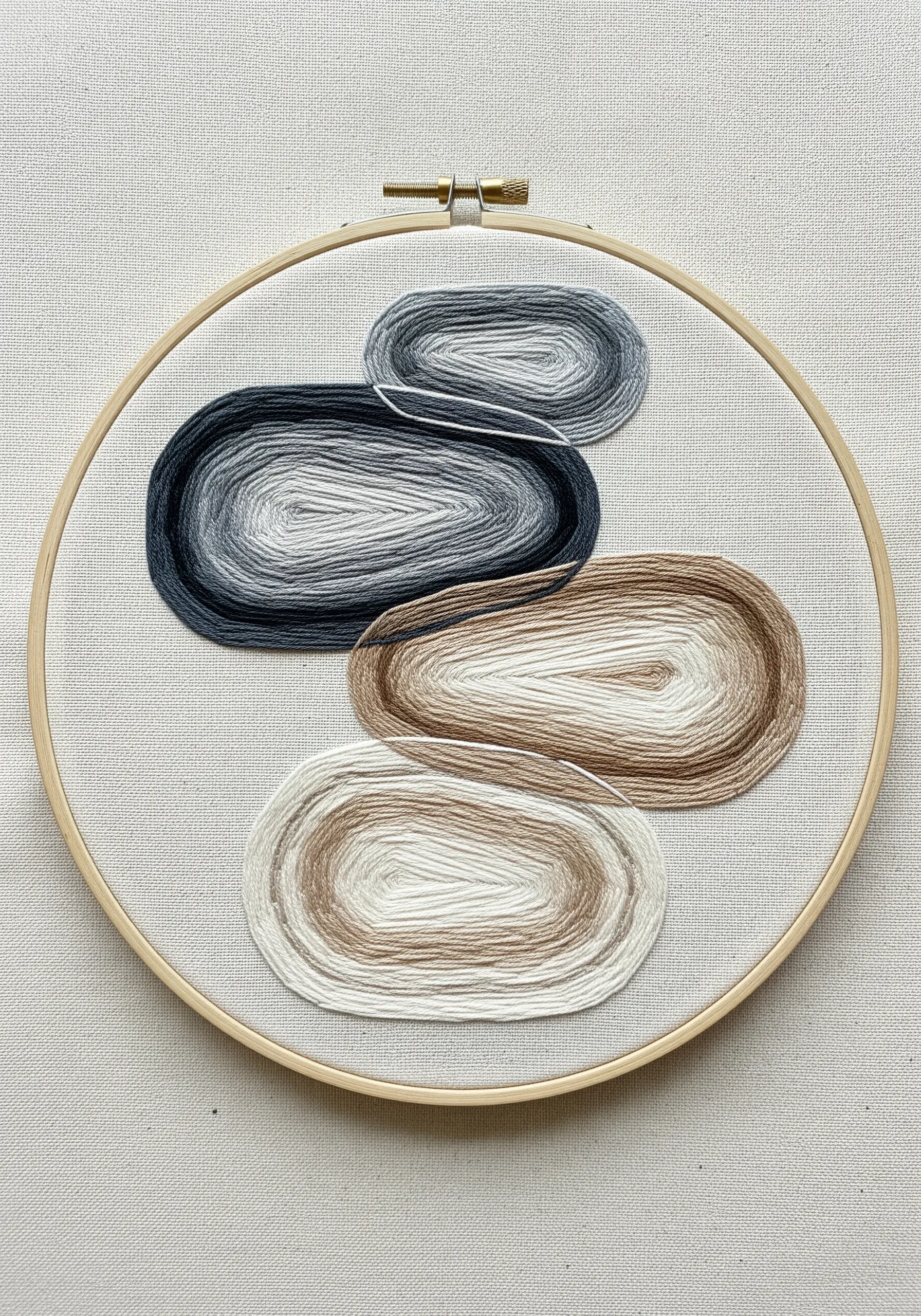 Abstract pebble shapes embroidered with concentric rings of neutral-toned split stitch.