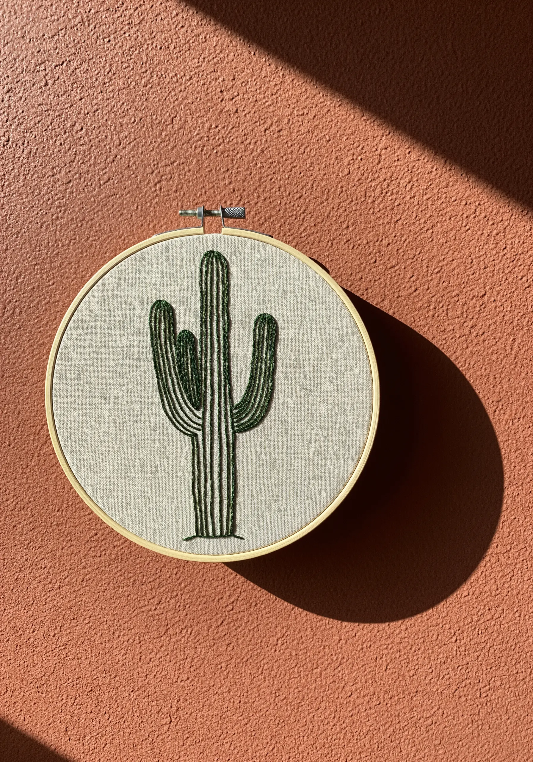Saguaro cactus embroidery with vertical green stripes on a light fabric, lit by sunlight.