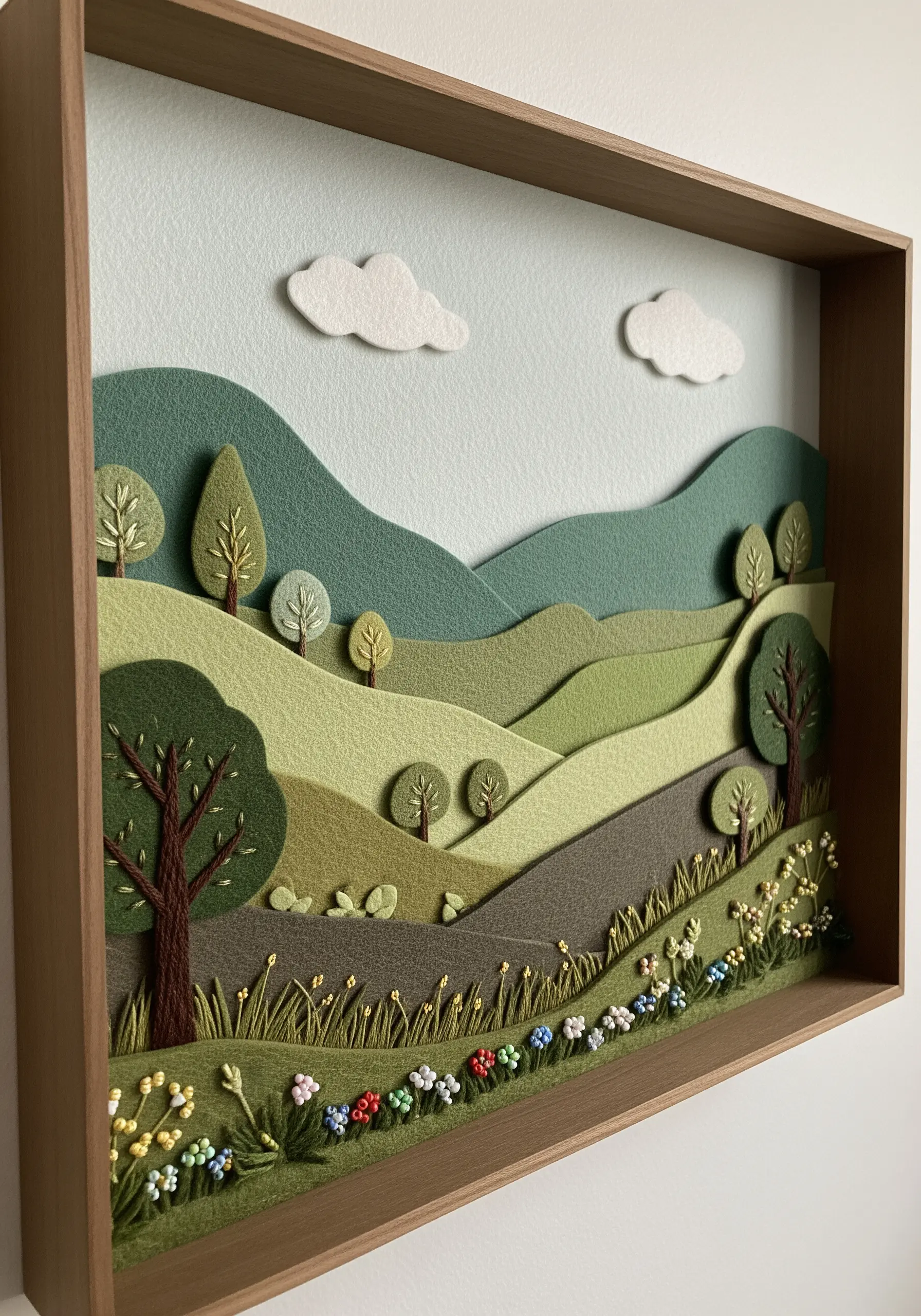 A shadow box landscape made with layers of green felt for hills and detailed embroidery in the foreground.