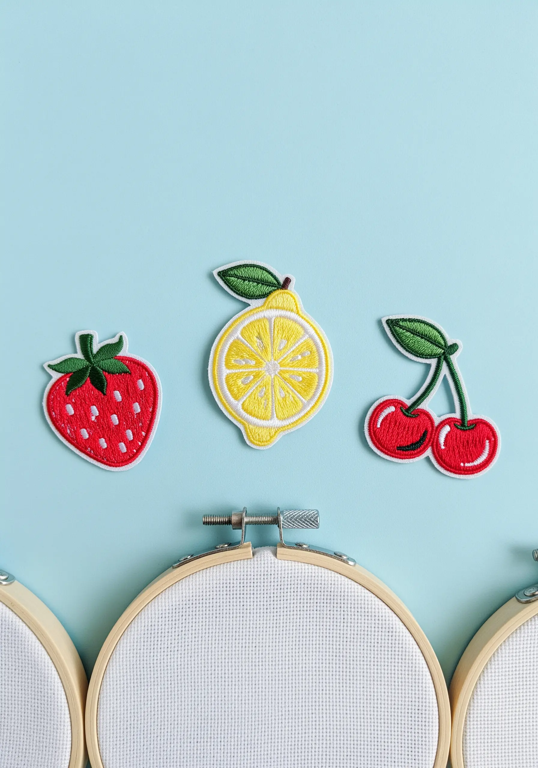 Three embroidered fruit patches—a strawberry, lemon, and cherry—ready to be applied.