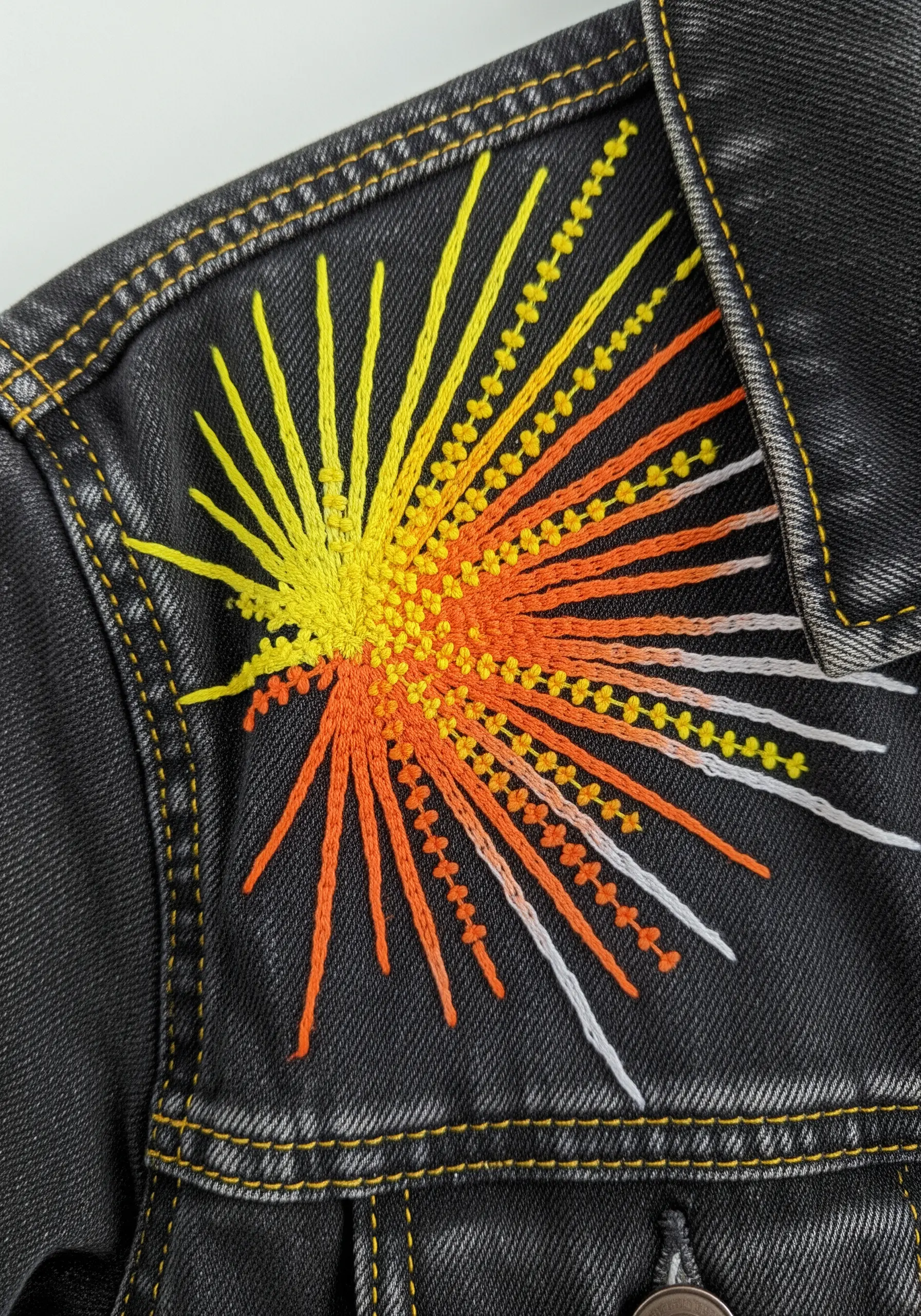 An abstract sunburst on a black denim jacket using French knots and radiating straight stitches.