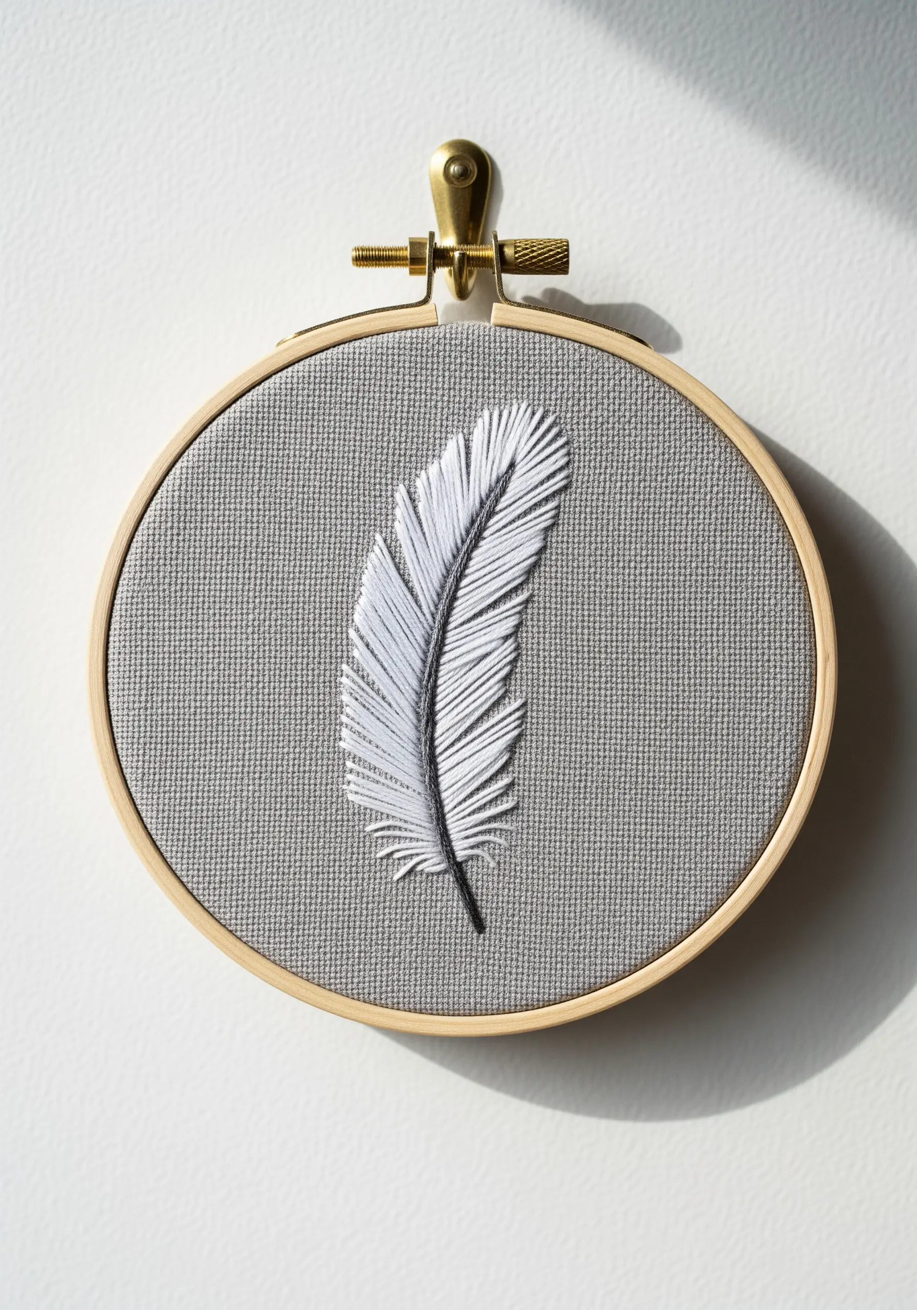 A realistic white and grey feather created with long-and-short stitch on grey fabric.