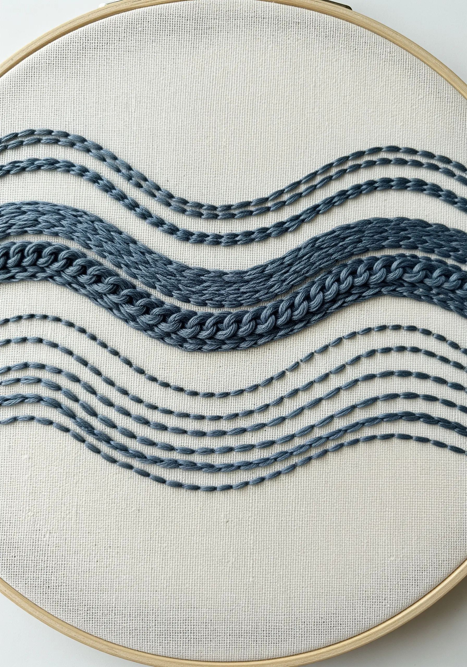 Embroidery hoop with parallel wavy lines stitched in different textures like chain and running stitch.