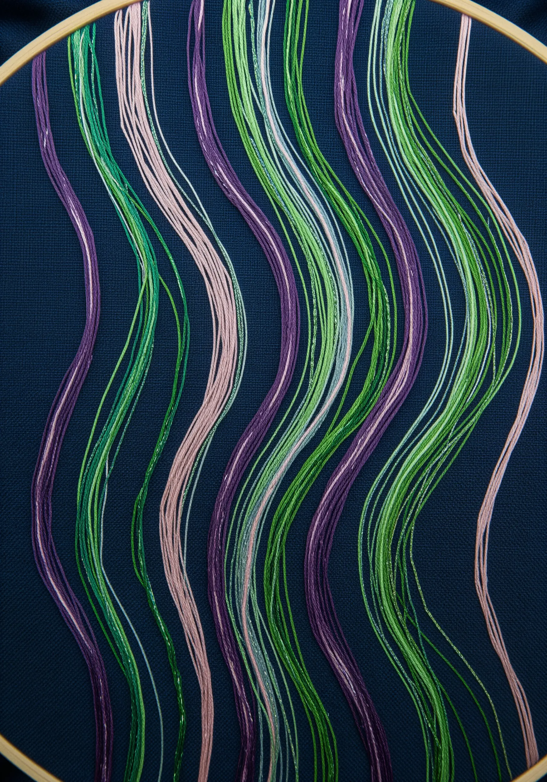 Long, wavy stitches in green, purple, and cream on dark blue fabric.