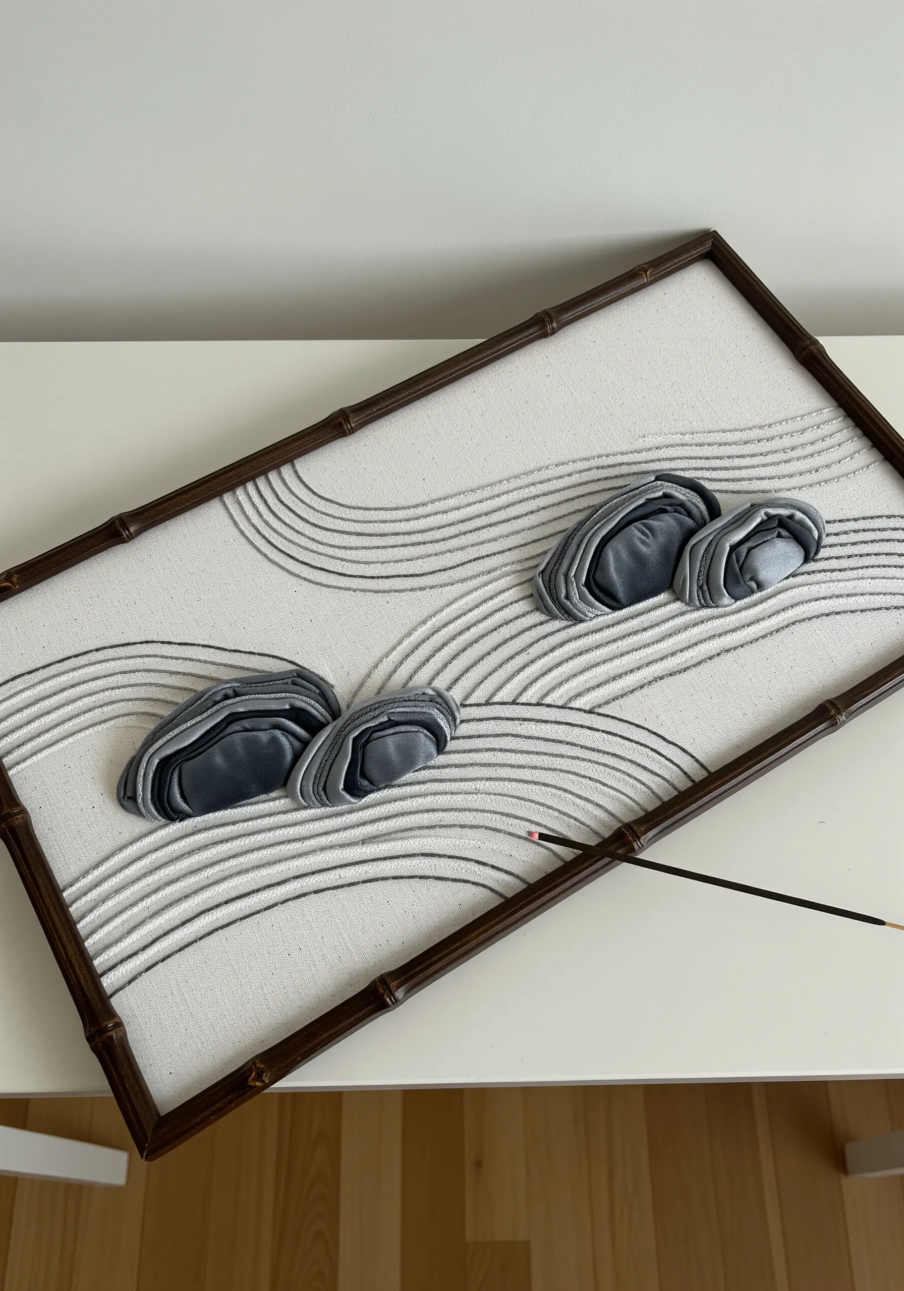 A framed textile art piece of a zen garden with 3D satin rocks and stitched sand lines.