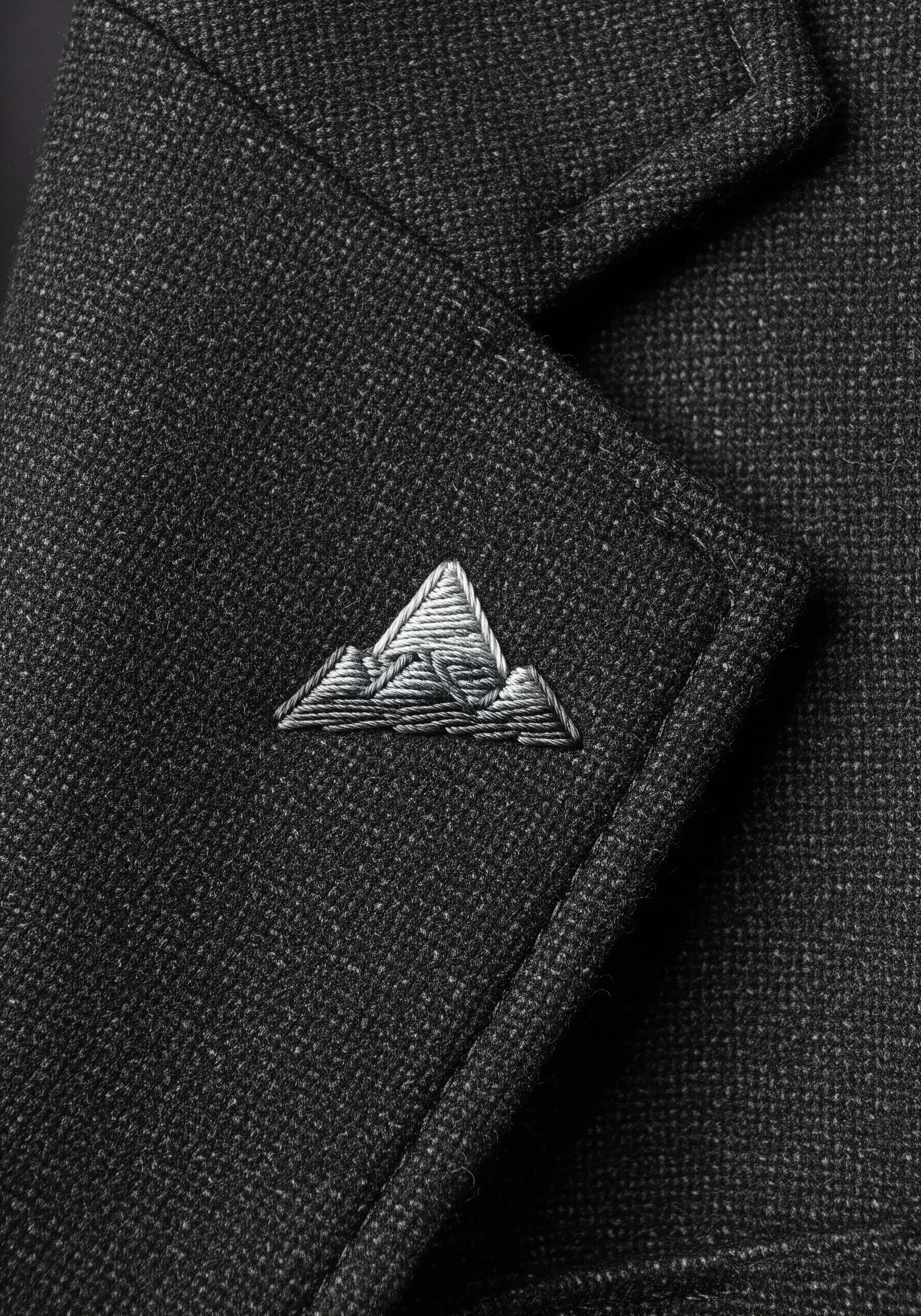 A tiny, intricately shaded mountain peak embroidered on the lapel of a dark wool blazer.