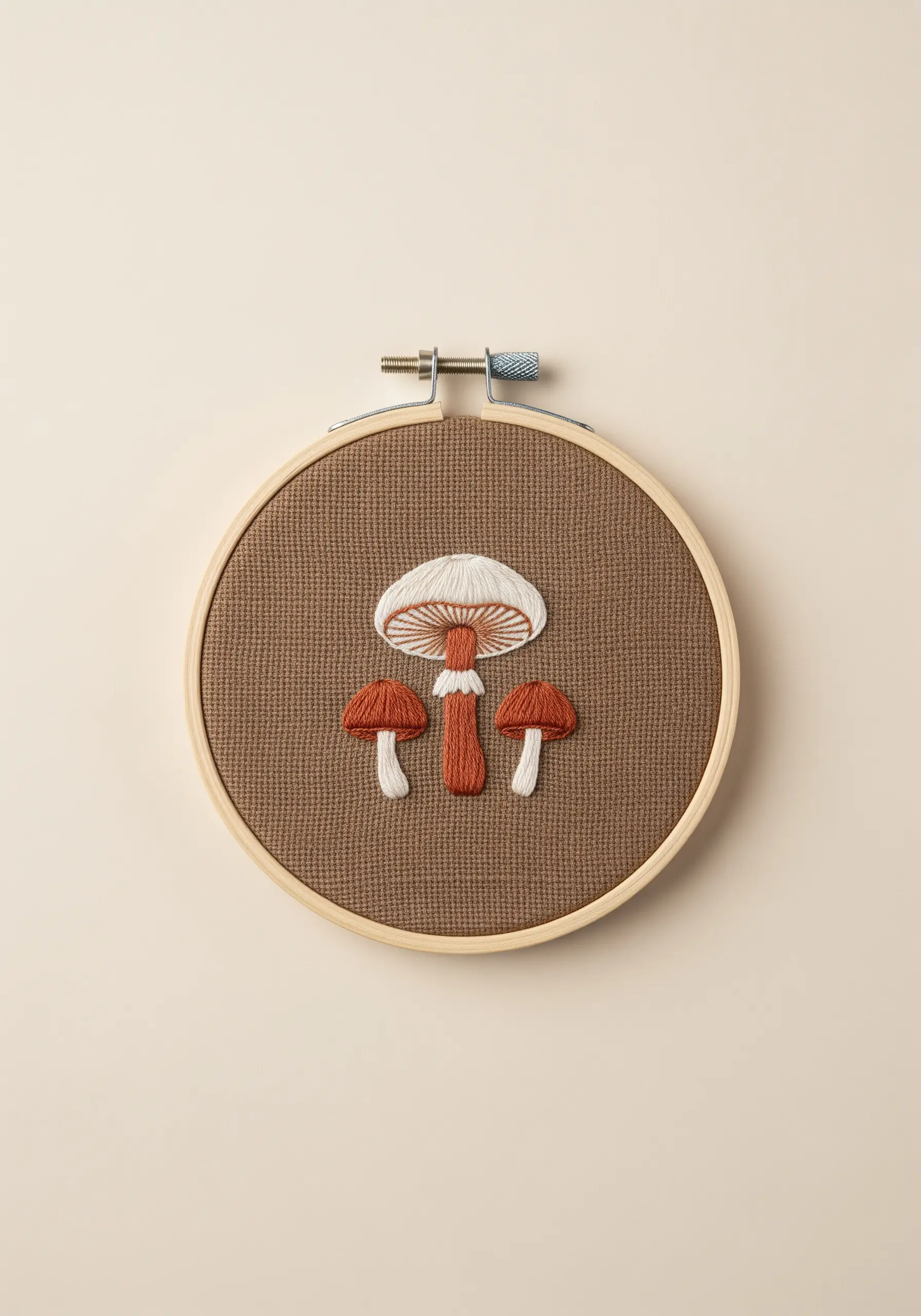 Three embroidered mushrooms with detailed, color-blended gills on brown Aida cloth.